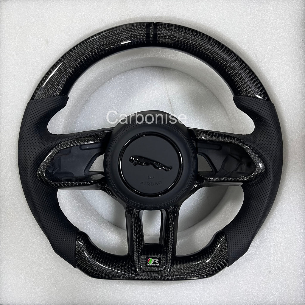 Custom Jaguar R carbon fibre steering wheel with black perforated leather grips, gloss carbon trim, centre stripe, and flat-bottom performance design.