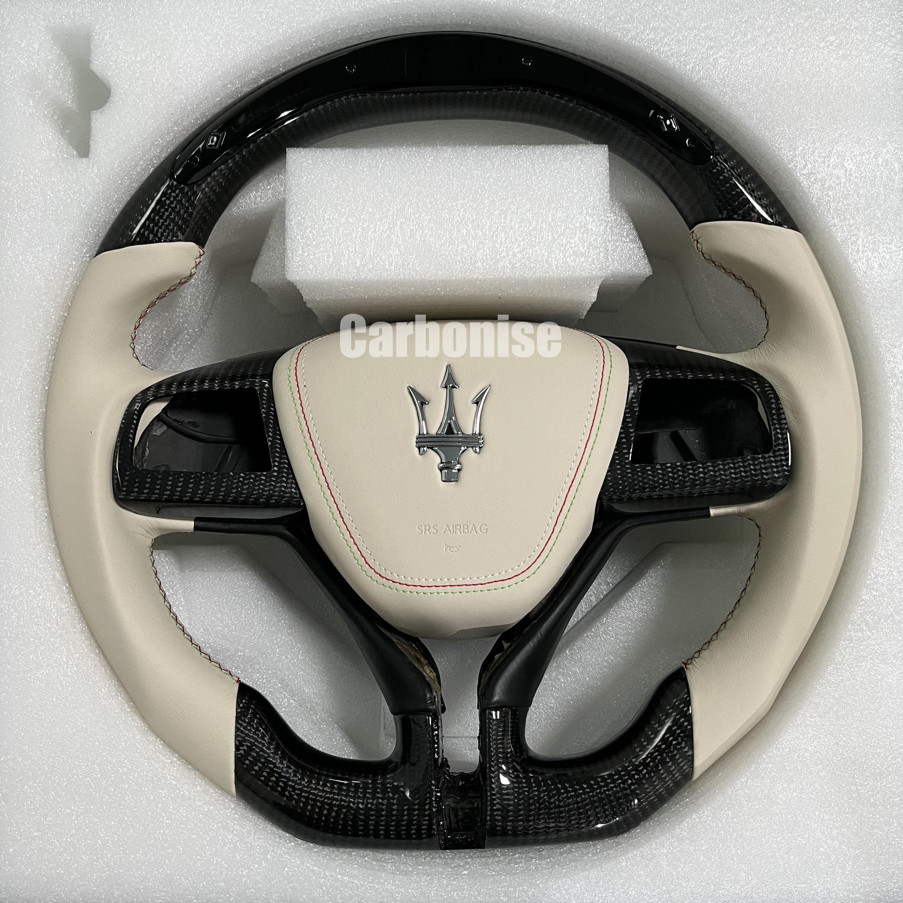 Custom Maserati carbon fibre steering wheel with beige leather side grips, contrast stitching, gloss carbon trim, and a flat-bottom luxury performance design.