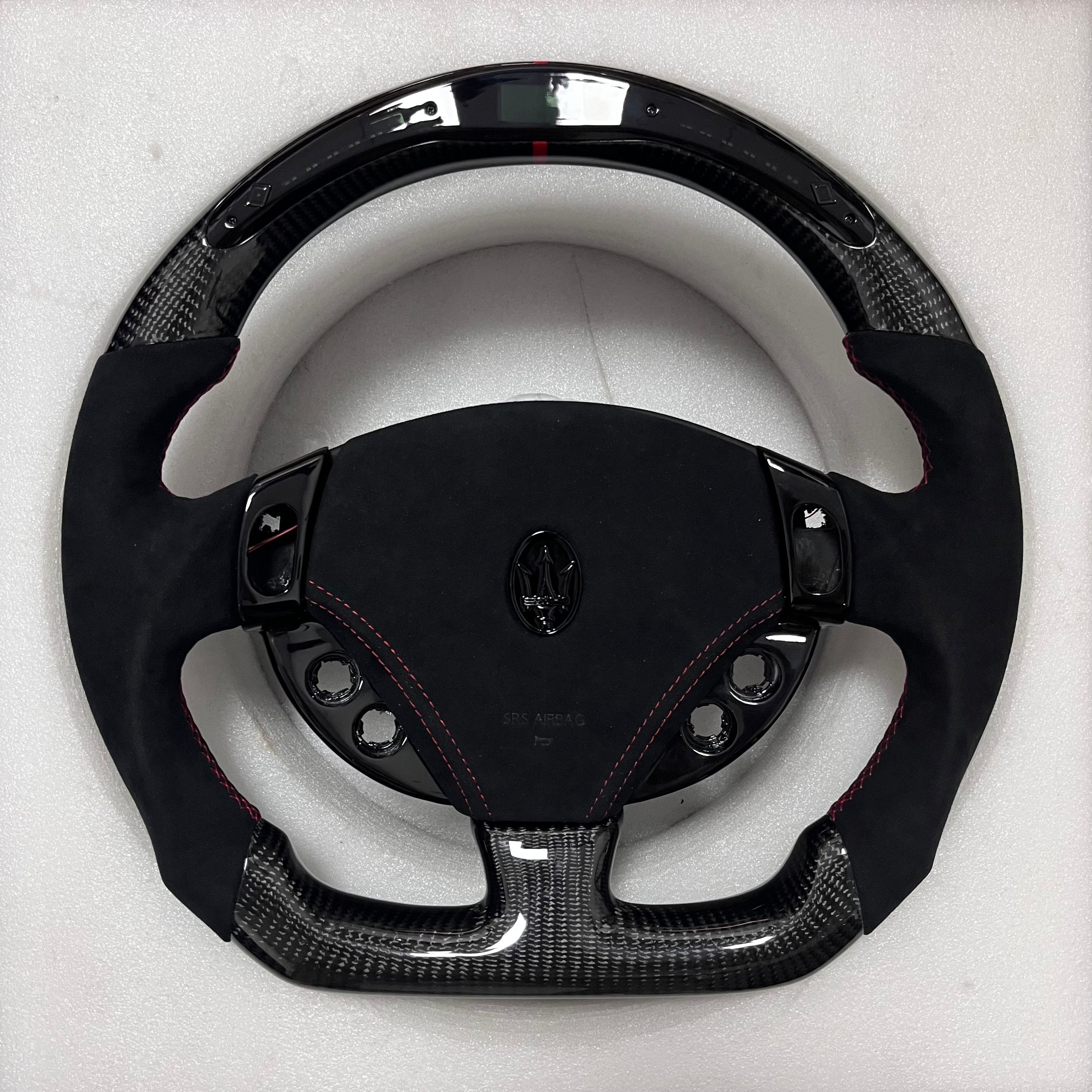 Custom Maserati carbon fibre steering wheel with black Alcantara side grips, red contrast stitching, gloss carbon trim, and a flat-bottom performance shape. Led Shift light