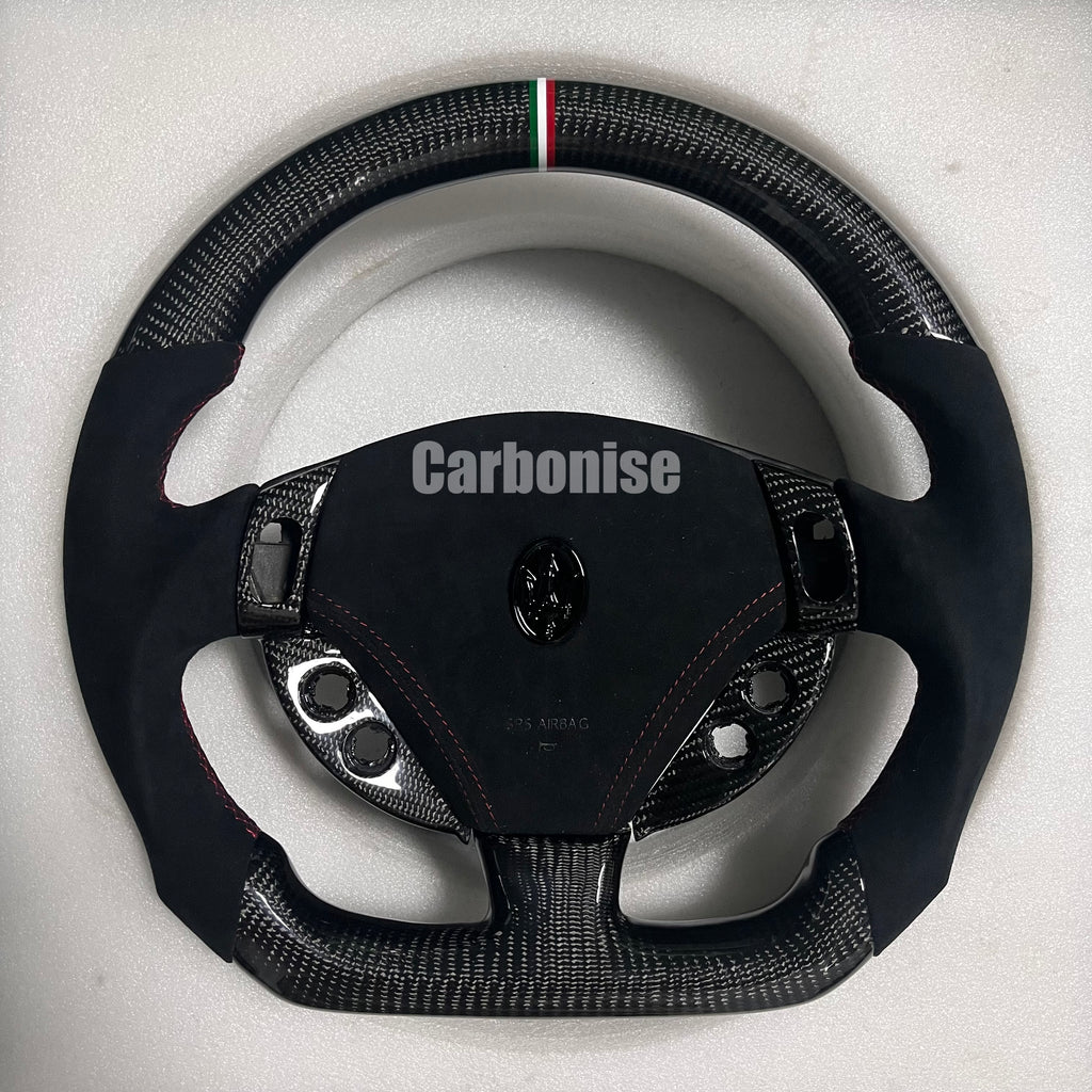 Custom Maserati carbon fibre steering wheel with black Alcantara side grips, red contrast stitching, Italian tricolour centre stripe, and flat-bottom design.
