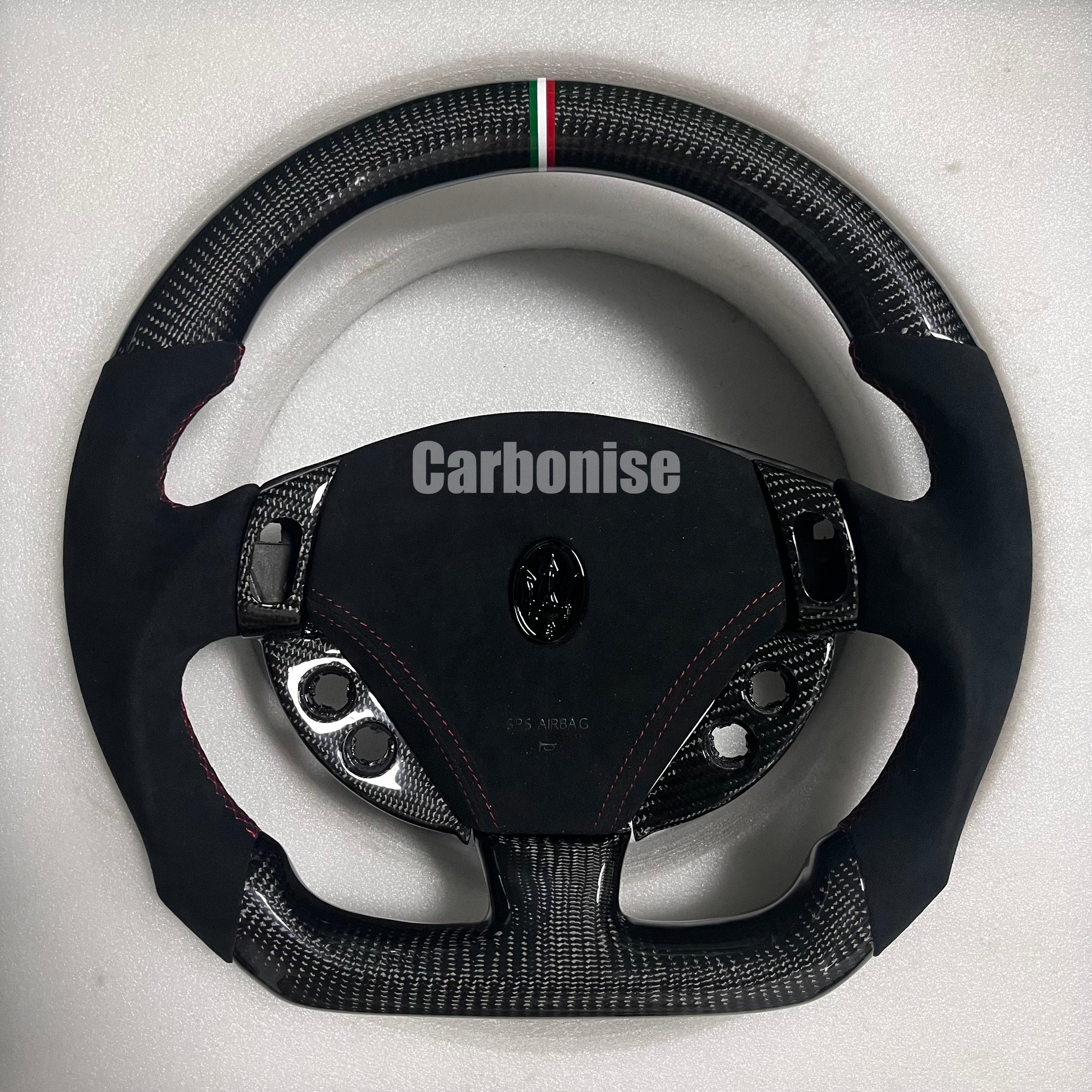 Custom Maserati carbon fibre steering wheel with black Alcantara side grips, red contrast stitching, Italian tricolour centre stripe, and flat-bottom design.