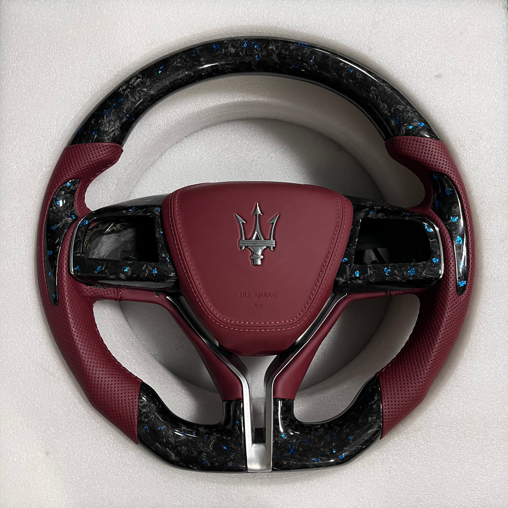 Custom Maserati forged carbon steering wheel with blue flake carbon fibre, burgundy perforated leather grips, burgundy airbag cover, and flat-bottom shape.
