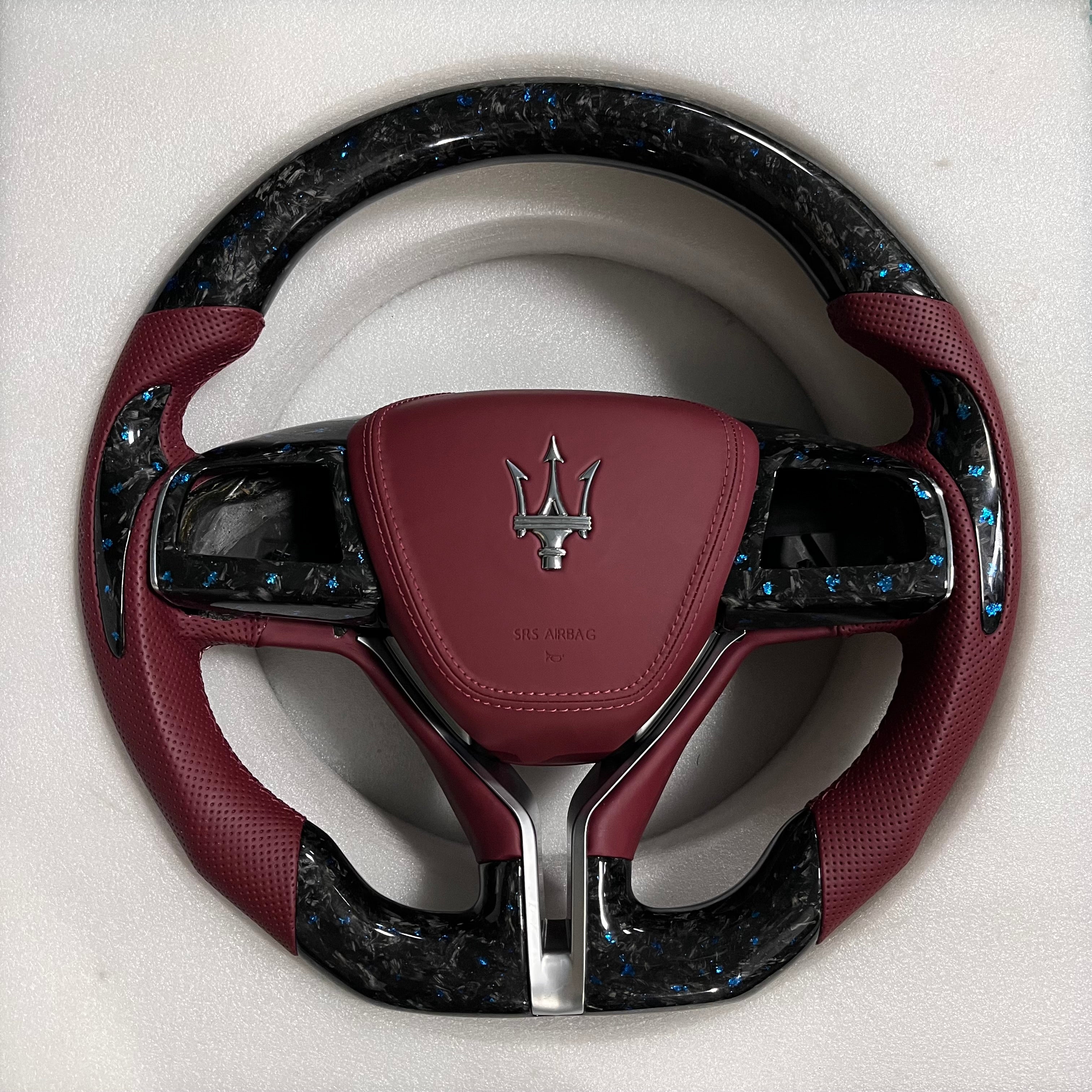 Custom Maserati forged carbon steering wheel with blue flake carbon fibre, burgundy perforated leather grips, burgundy airbag cover, and flat-bottom shape.