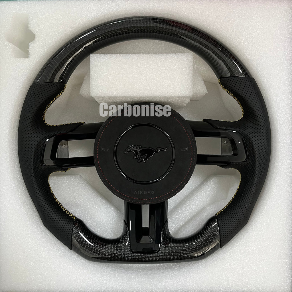 Ford Mustang carbon fibre steering wheel with perforated black leather grips, yellow stitching accents, round design, and OEM Mustang airbag cover.