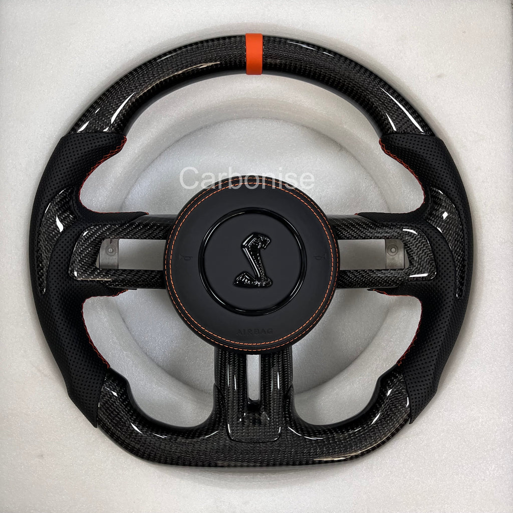 Ford Mustang Shelby carbon fibre steering wheel with perforated black leather grips, orange centre stripe, orange stitching, and Shelby Cobra airbag.