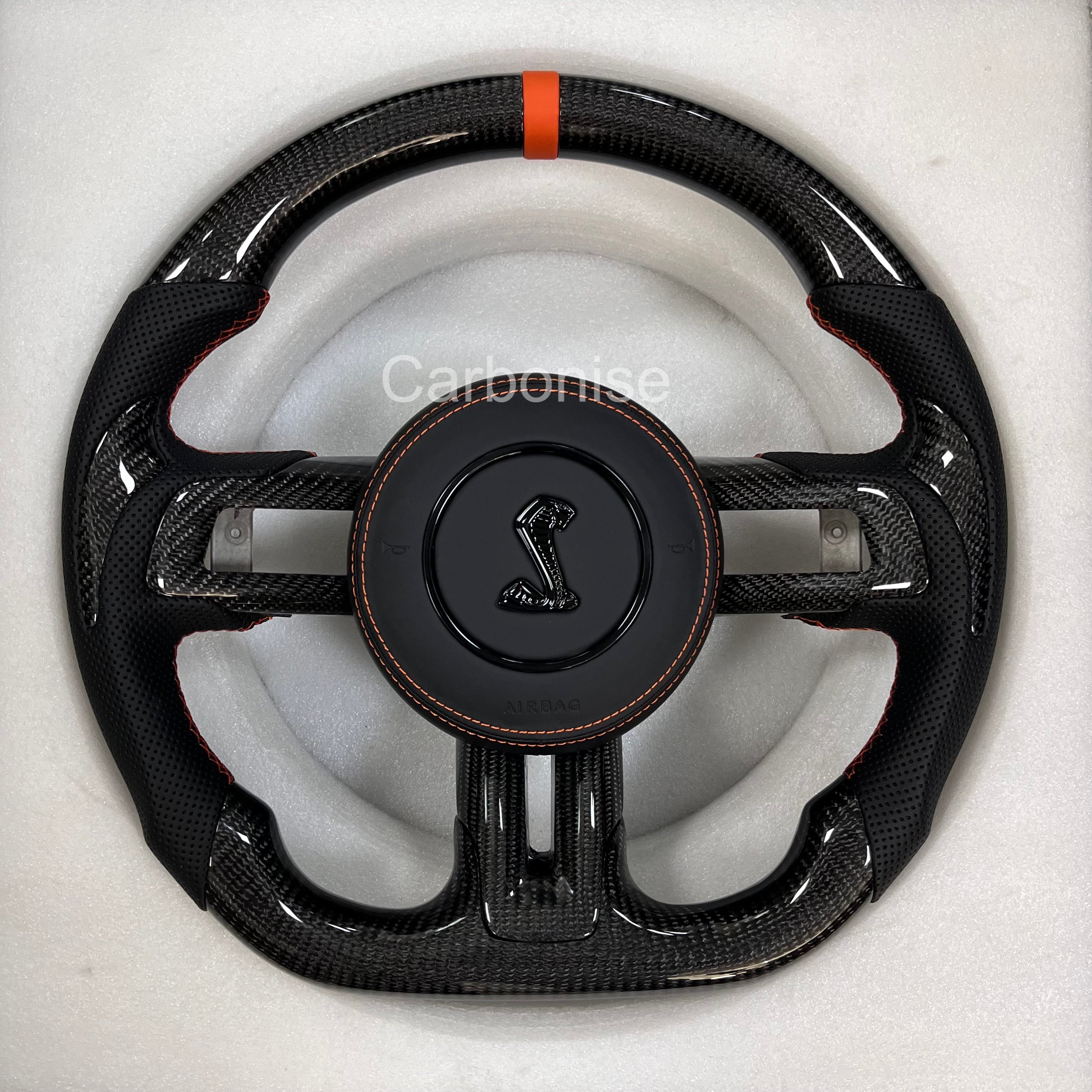 Ford Mustang Shelby carbon fibre steering wheel with perforated black leather grips, orange centre stripe, orange stitching, and Shelby Cobra airbag.