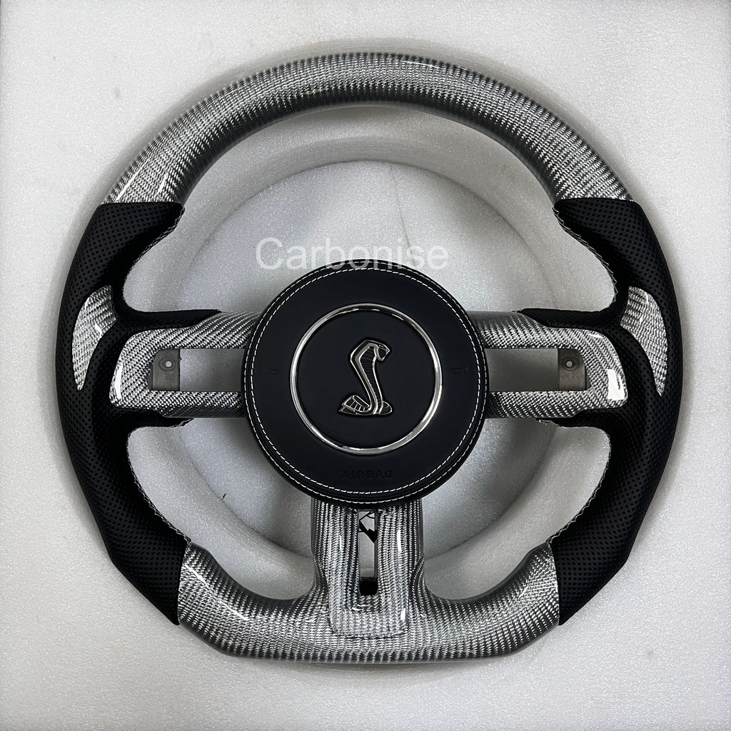 Ford Mustang carbon fibre steering wheel with silver forged carbon finish, perforated black leather grips, round design, and Shelby Cobra airbag.