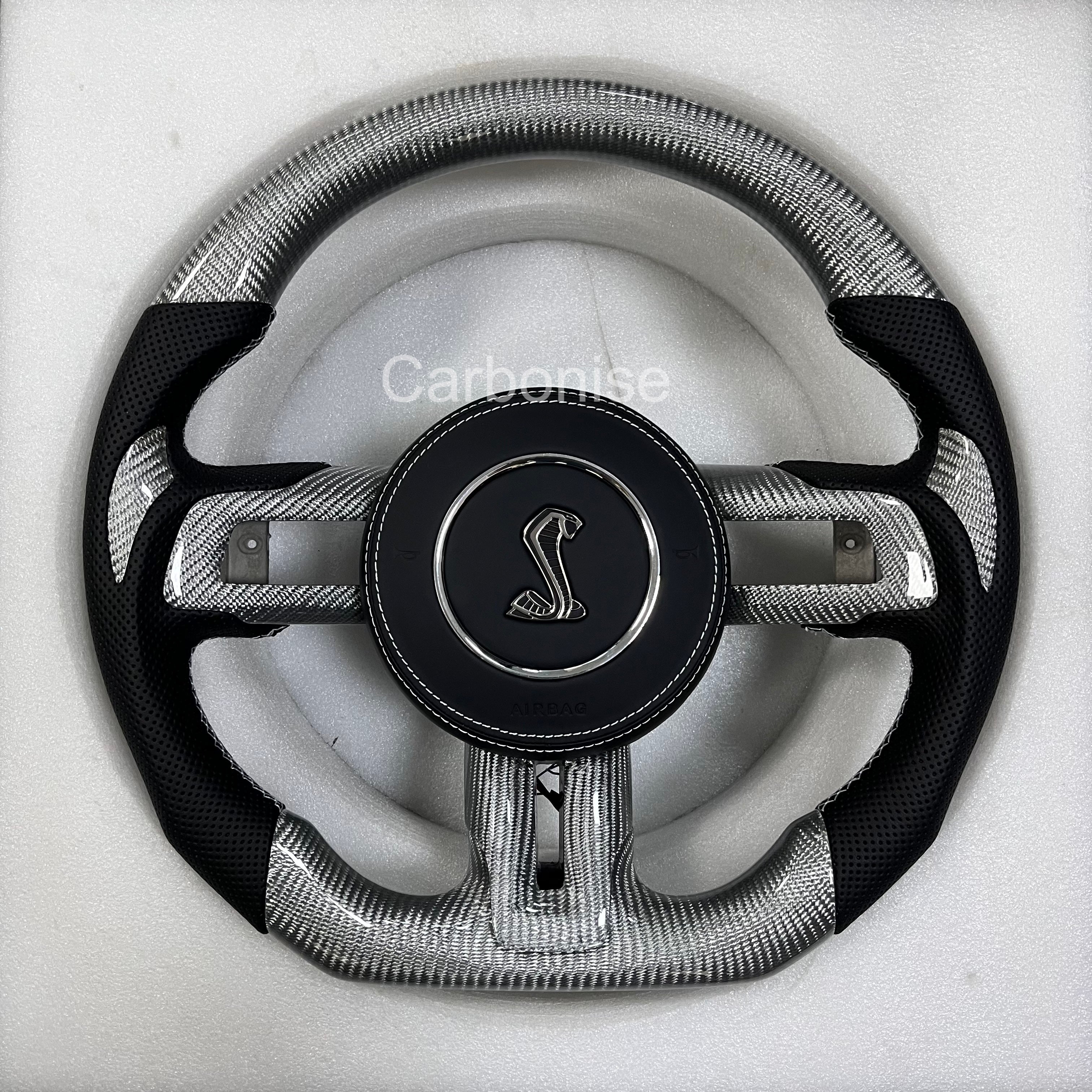 Ford Mustang carbon fibre steering wheel with silver forged carbon finish, perforated black leather grips, round design, and Shelby Cobra airbag.