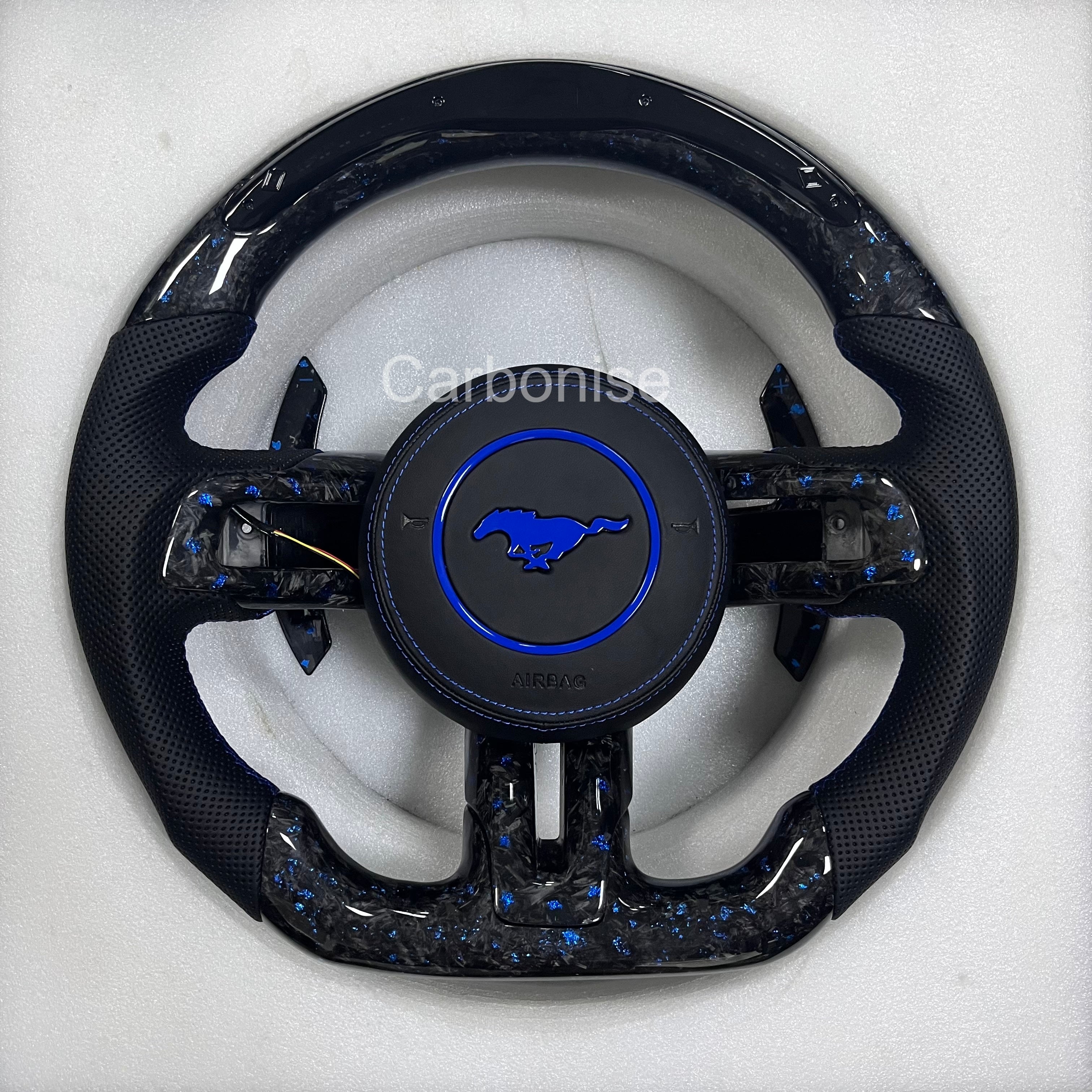 Ford Mustang forged carbon fibre steering wheel with blue metallic flakes, perforated black leather grips, blue accent airbag ring, matching forged carbon spokes, and OEM Mustang pony airbag.