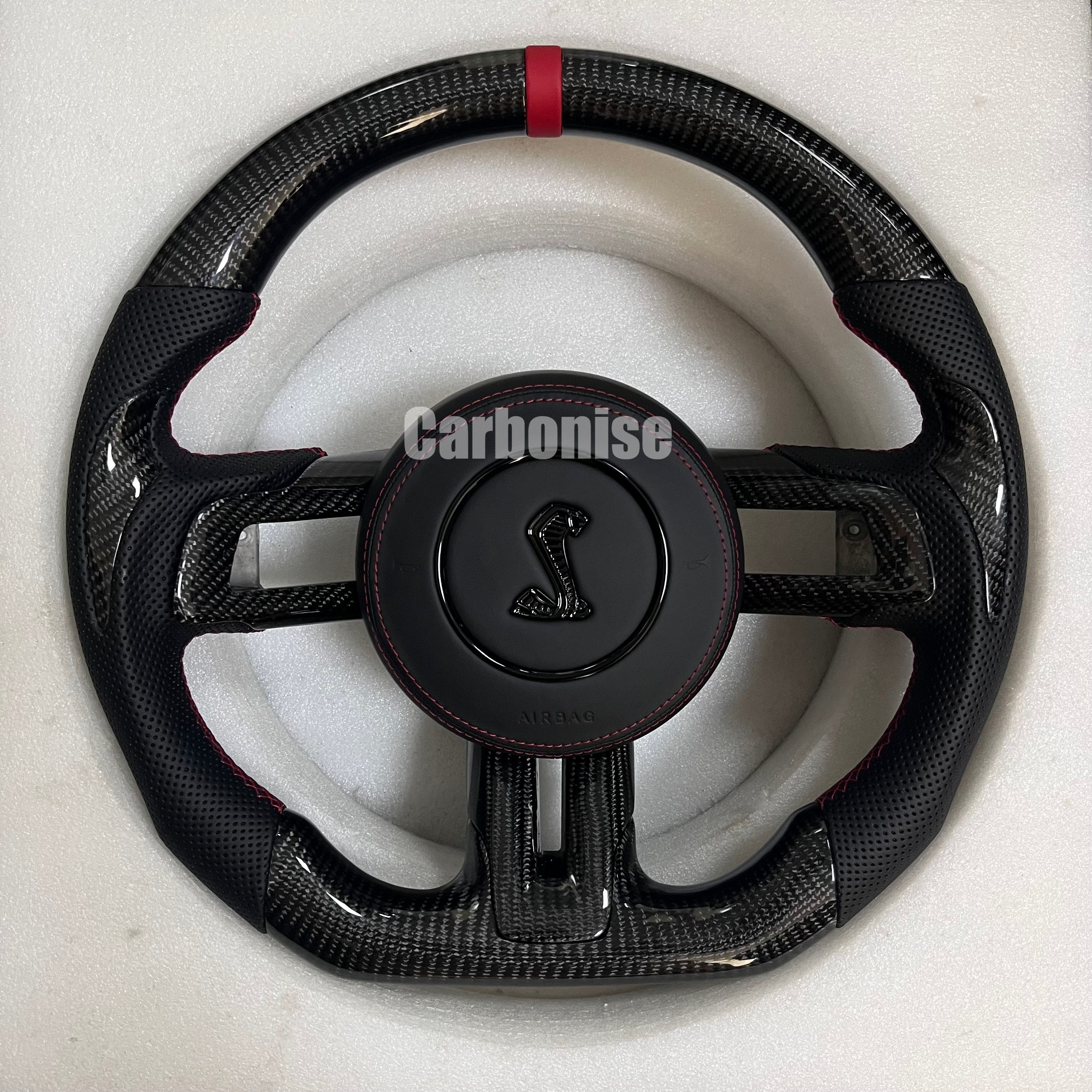 Ford Mustang carbon fibre steering wheel with red centre stripe, perforated black leather grips, red stitching, round design, and Shelby Cobra airbag.