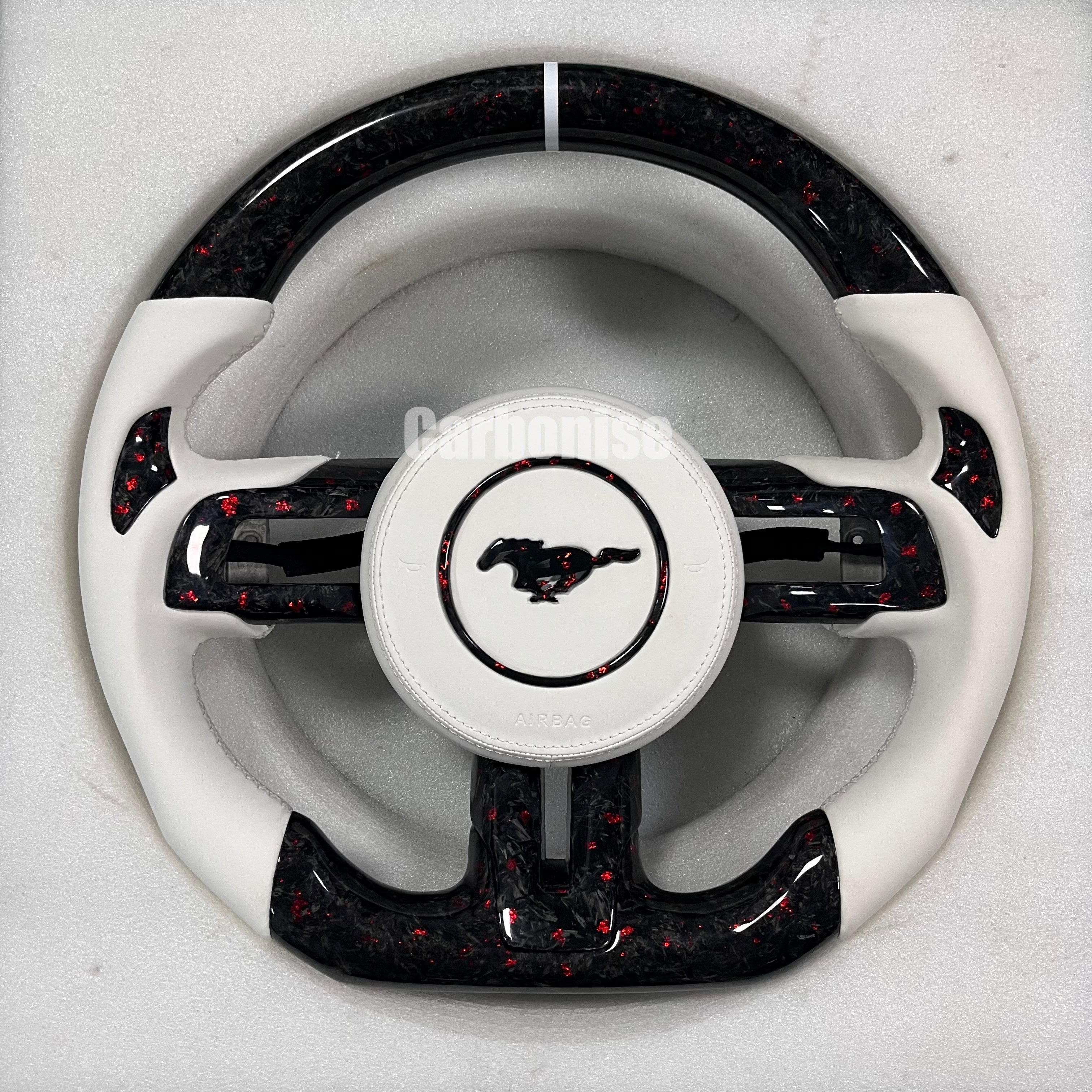 Ford Mustang forged carbon fibre steering wheel with red flake finish, white leather side grips, white centre stripe, matching forged carbon spokes, and white Mustang pony airbag.