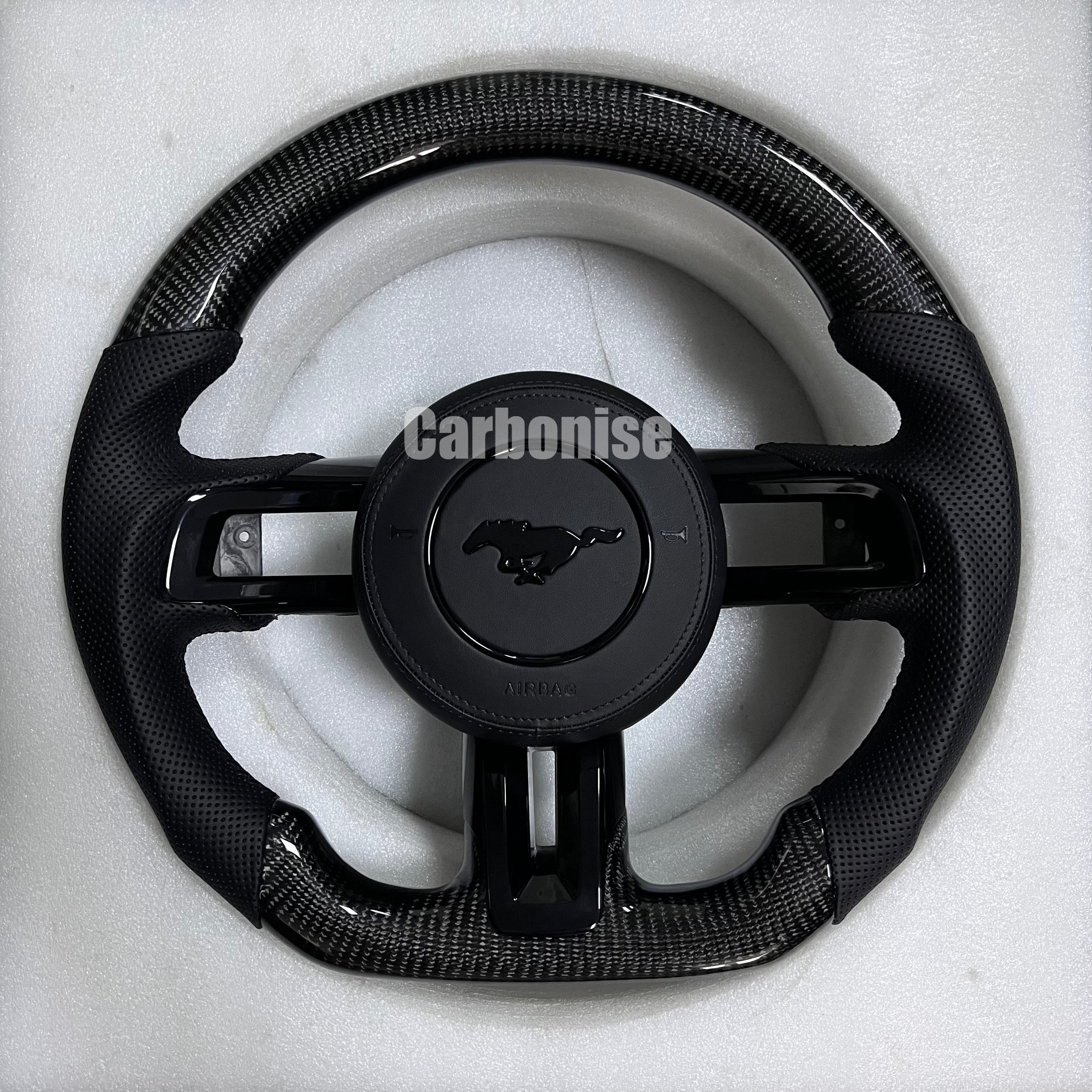 Ford Mustang carbon fibre steering wheel with gloss black carbon top and bottom, perforated black leather grips, matching centre spokes, round design, and OEM Mustang pony airbag.