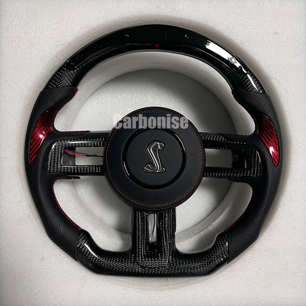 Ford Mustang Shelby carbon fibre steering wheel with red carbon accent inlays, perforated black leather grips, red stitching, gloss black carbon top and bottom, and Shelby Cobra airbag.