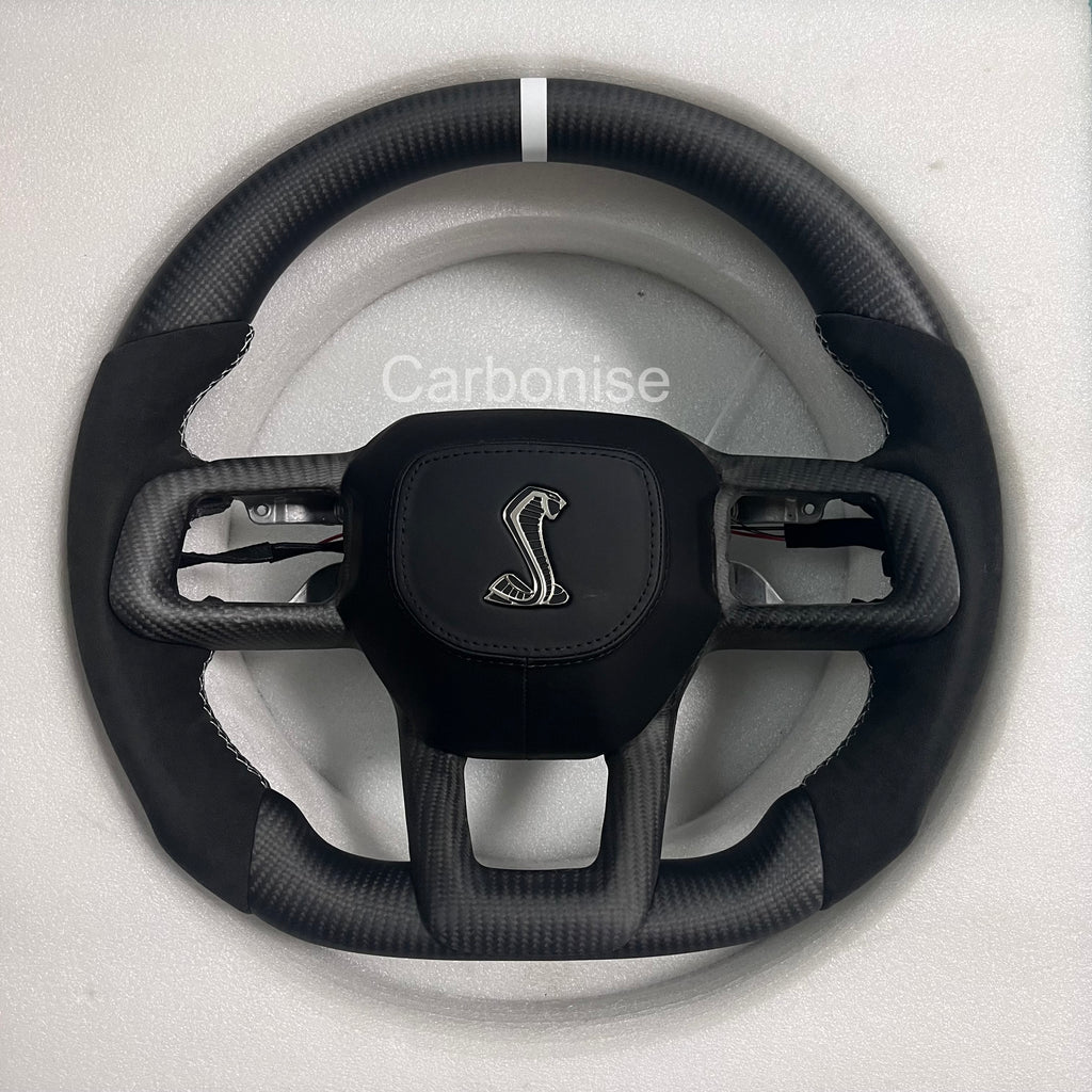 Ford Mustang Shelby matte carbon fibre steering wheel with Alcantara side grips, white centre stripe, round design, and Shelby Cobra airbag.