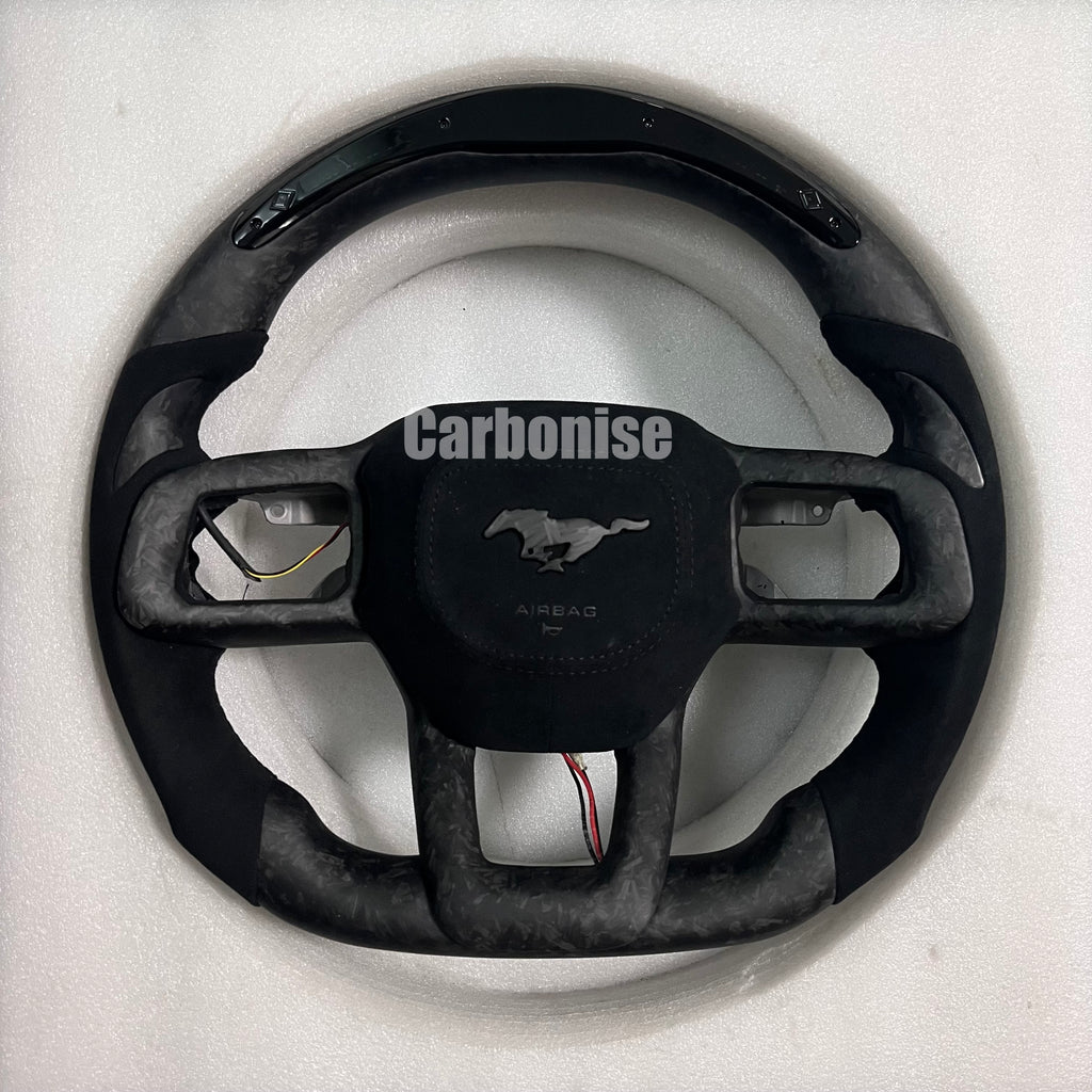 Ford Mustang matte forged carbon fibre steering wheel with Alcantara side grips, dark marbled finish, matching centre spokes, round design, and OEM Mustang pony airbag.