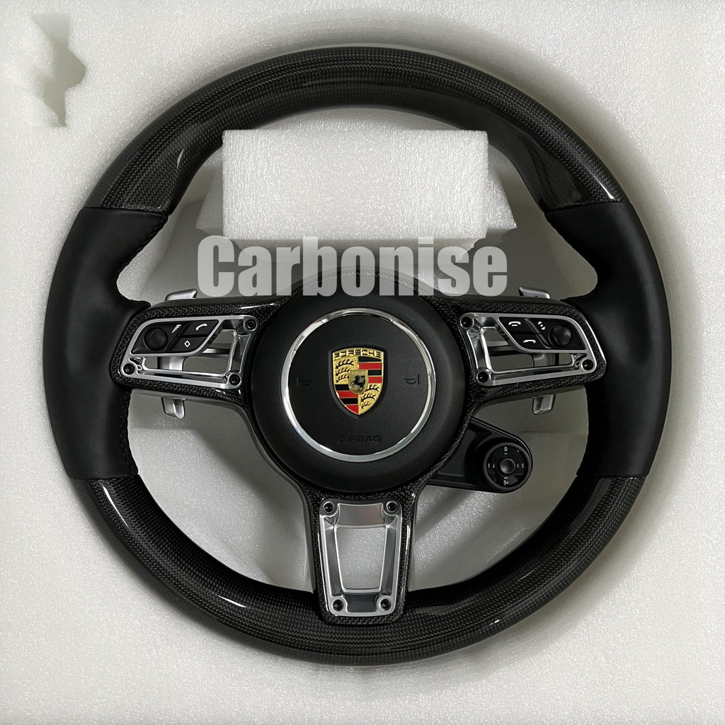 Custom Porsche performance steering wheel featuring high-gloss carbon fiber, integrated silver control hardware, and black smooth leather side grips.