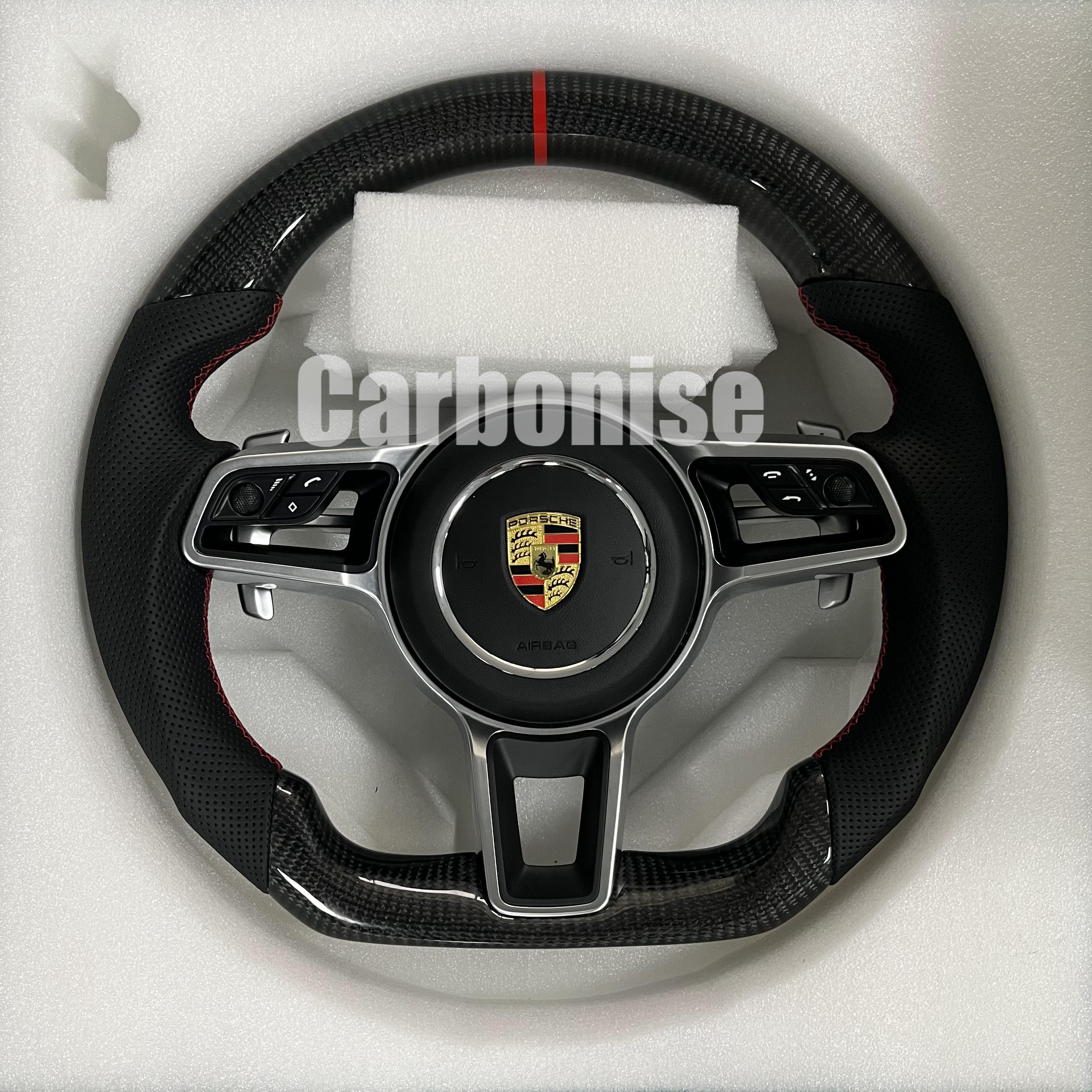 Custom Porsche performance steering wheel featuring high-gloss carbon fiber, a red top racing stripe, and integrated silver multi-function control hardware.