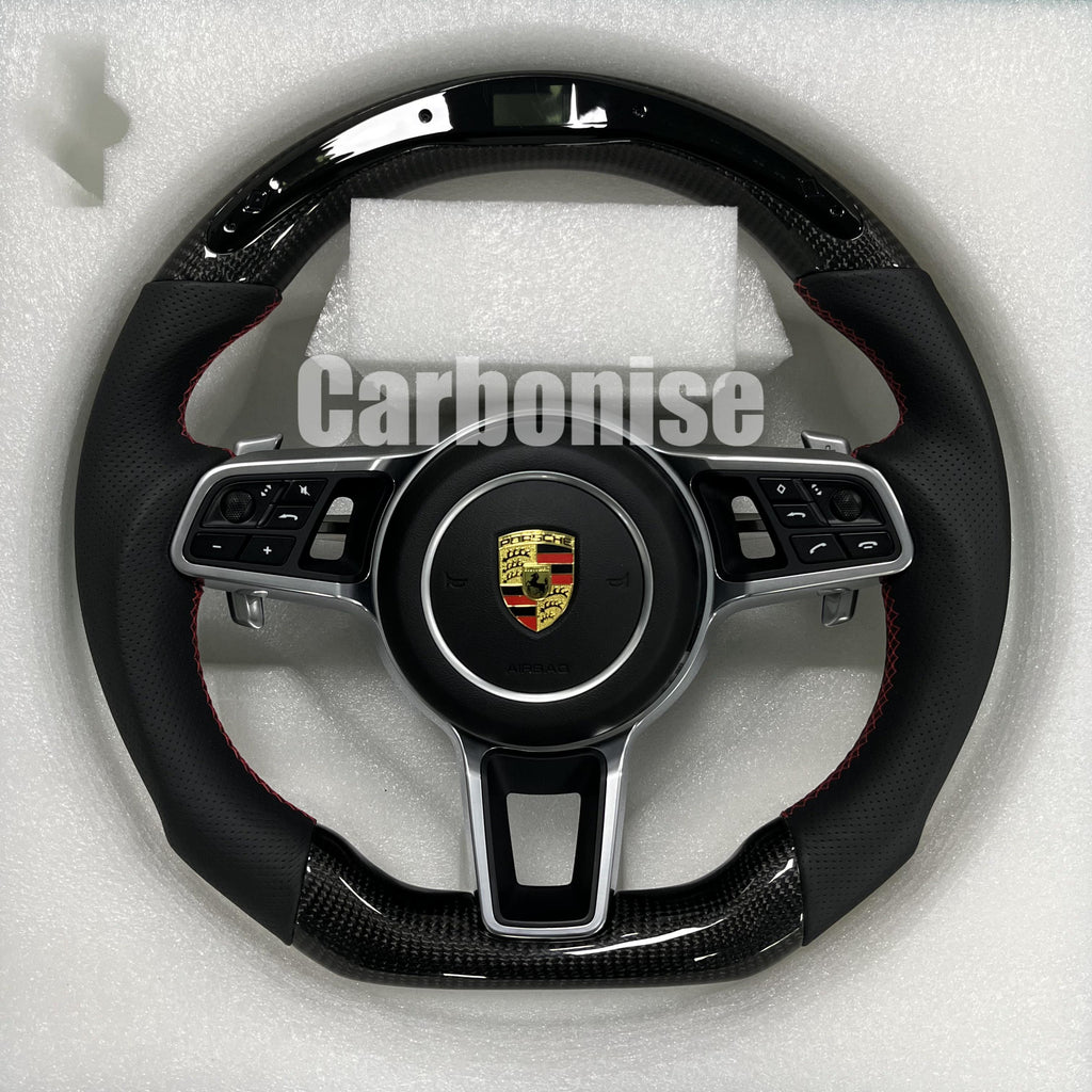 Custom Porsche performance steering wheel featuring high-gloss carbon fiber, an integrated LED shift indicator, and black perforated leather side grips with red stitching.