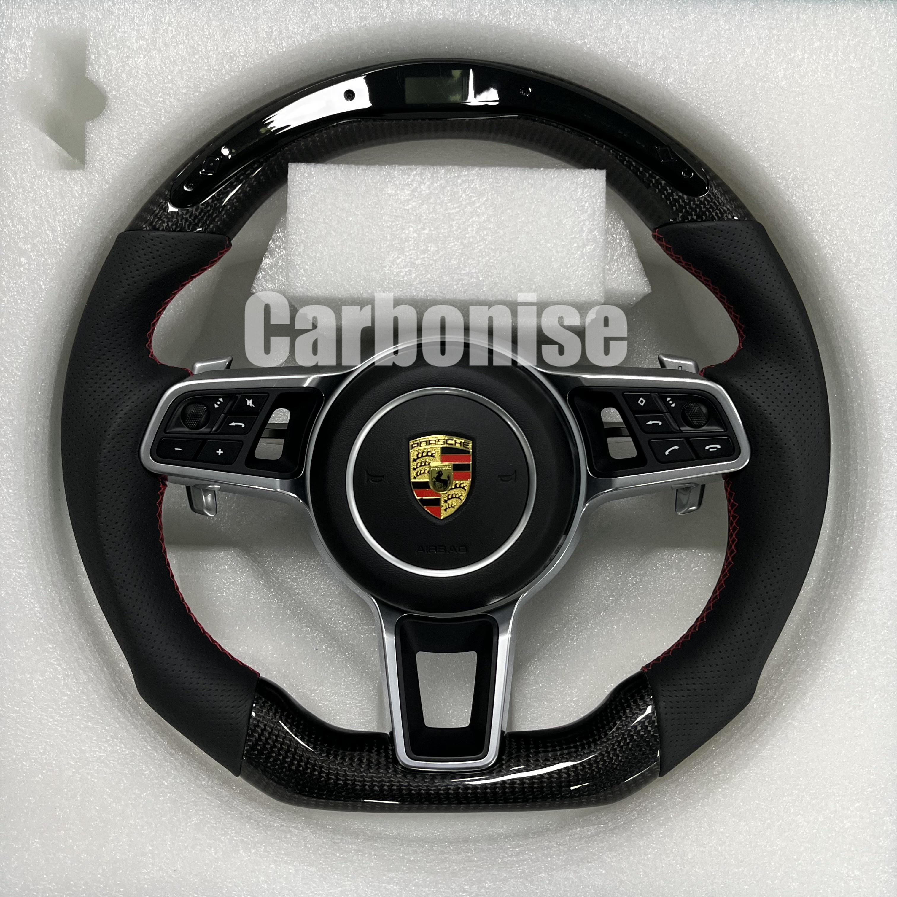 Custom Porsche performance steering wheel featuring high-gloss carbon fiber, an integrated LED shift indicator, and black perforated leather side grips with red stitching.