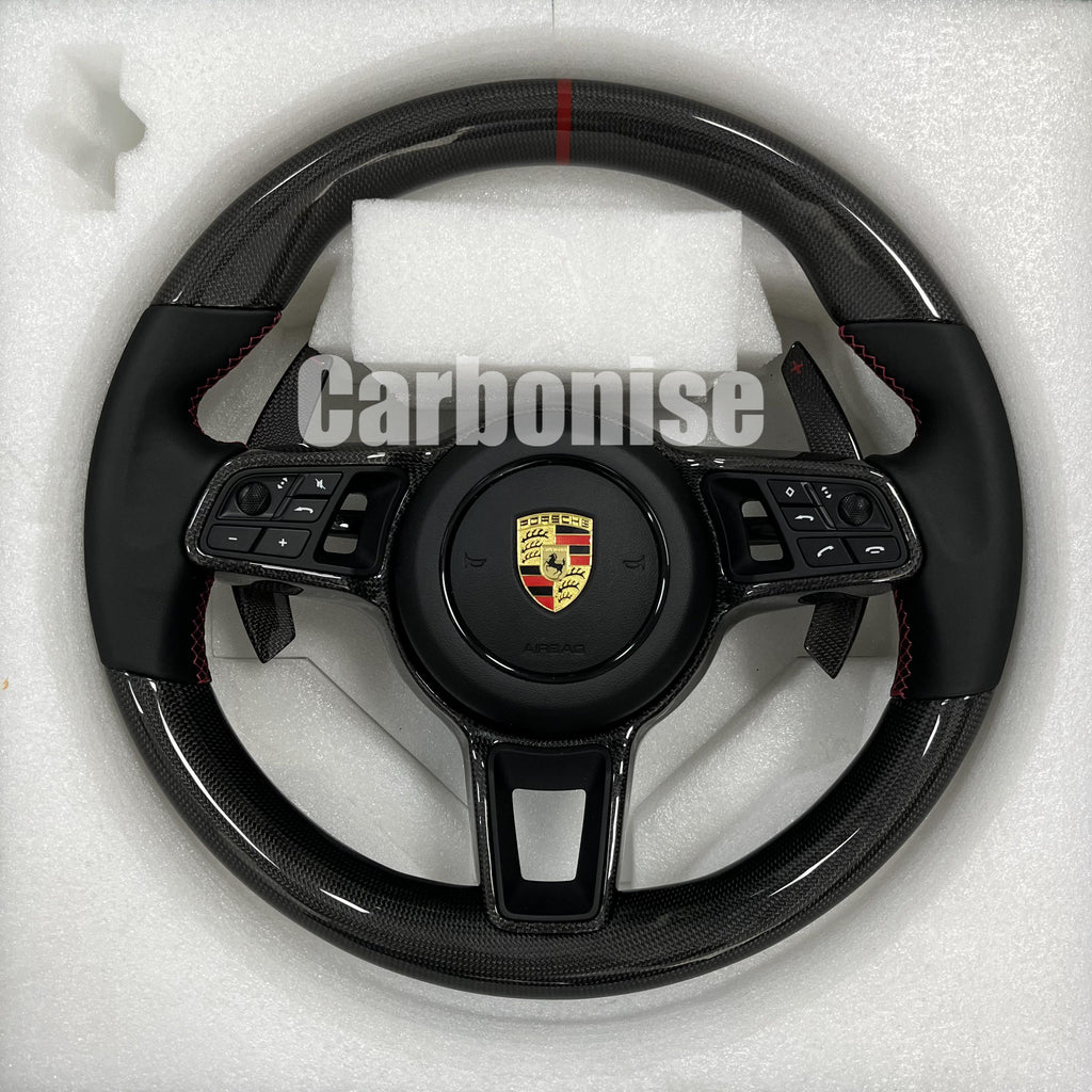 Custom Porsche performance steering wheel featuring high-gloss carbon fiber, a red top racing stripe, and black Alcantara side grips with red stitching.