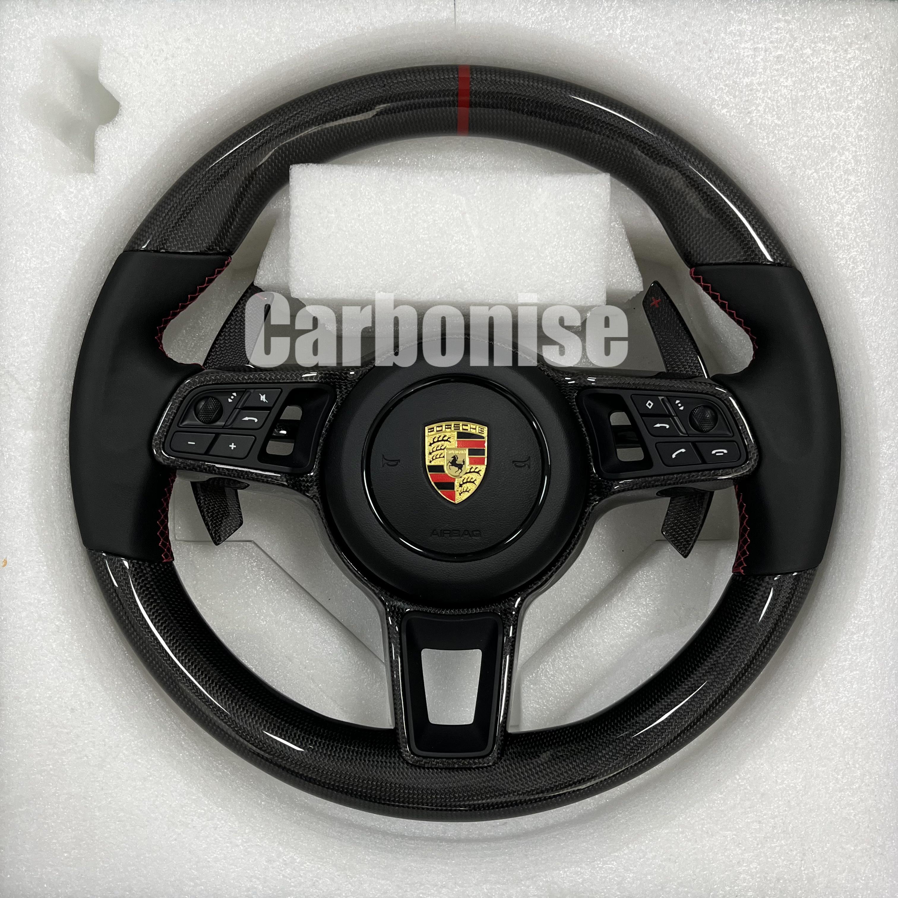 Custom Porsche performance steering wheel featuring high-gloss carbon fiber, a red top racing stripe, and black Alcantara side grips with red stitching.