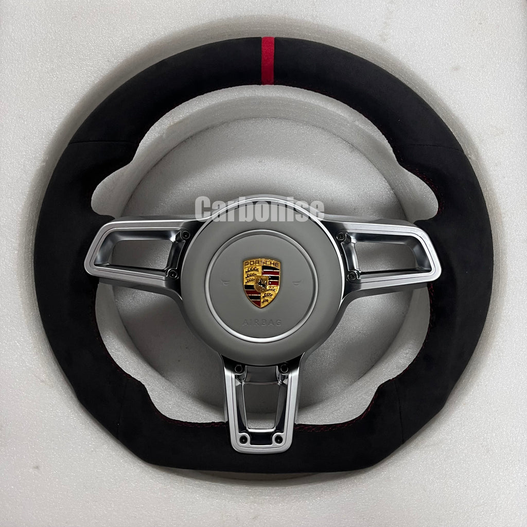 Custom Porsche performance steering wheel featuring a full black Alcantara wrap, a red top racing stripe, and silver multi-function control hardware.