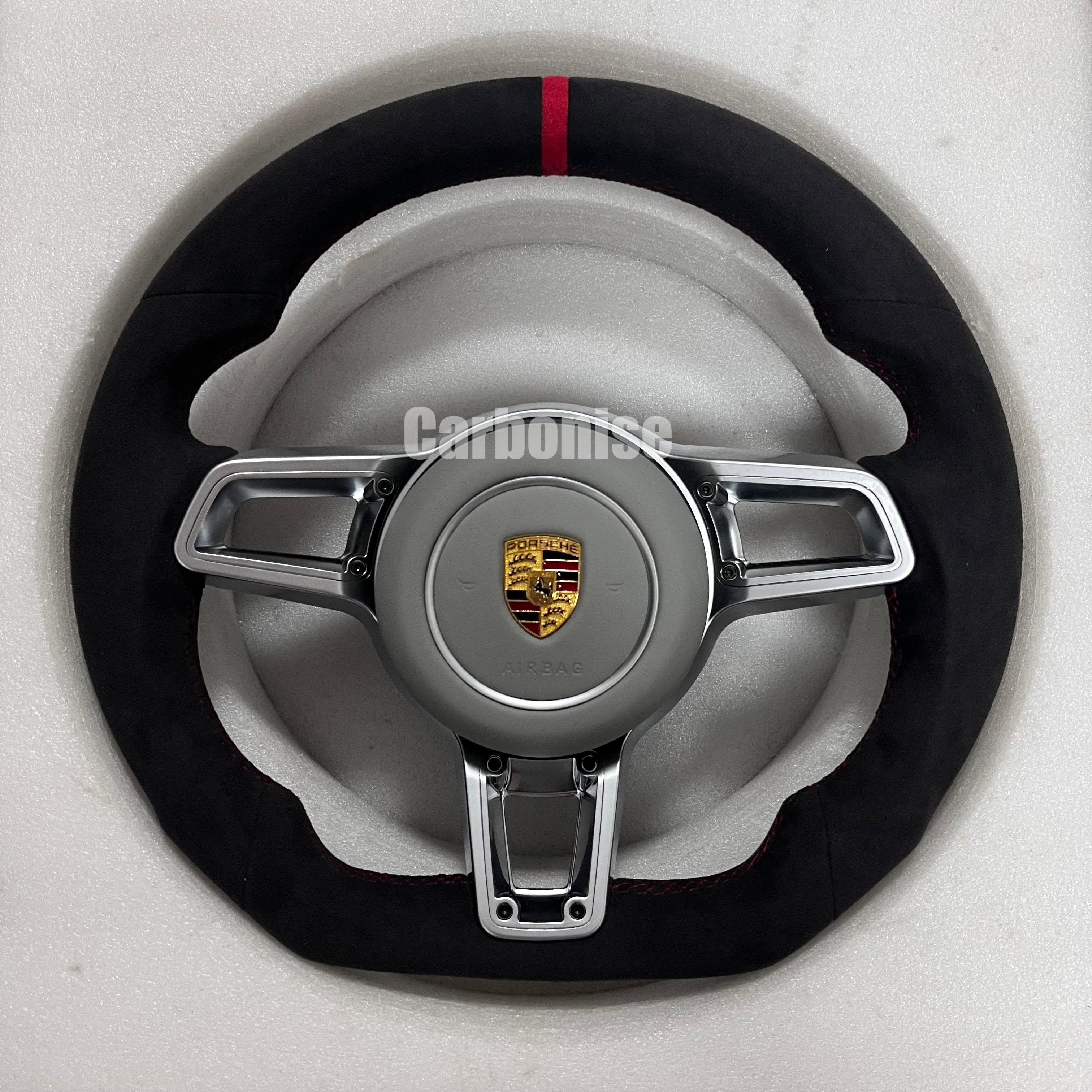 Custom Porsche performance steering wheel featuring a full black Alcantara wrap, a red top racing stripe, and silver multi-function control hardware.