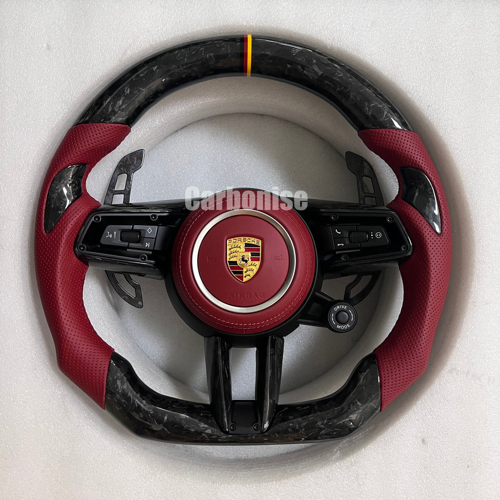 Custom Porsche performance steering wheel featuring high-gloss marbled forged carbon fiber, a tricolor top racing stripe, and red perforated leather side grips.