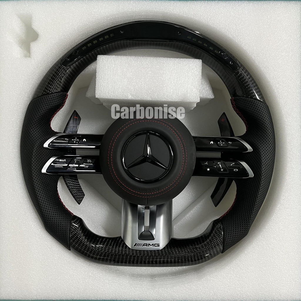 Custom Mercedes-Benz AMG performance steering wheel featuring high-gloss carbon fiber, a digital LED display, and perforated leather side grips with red stitching.