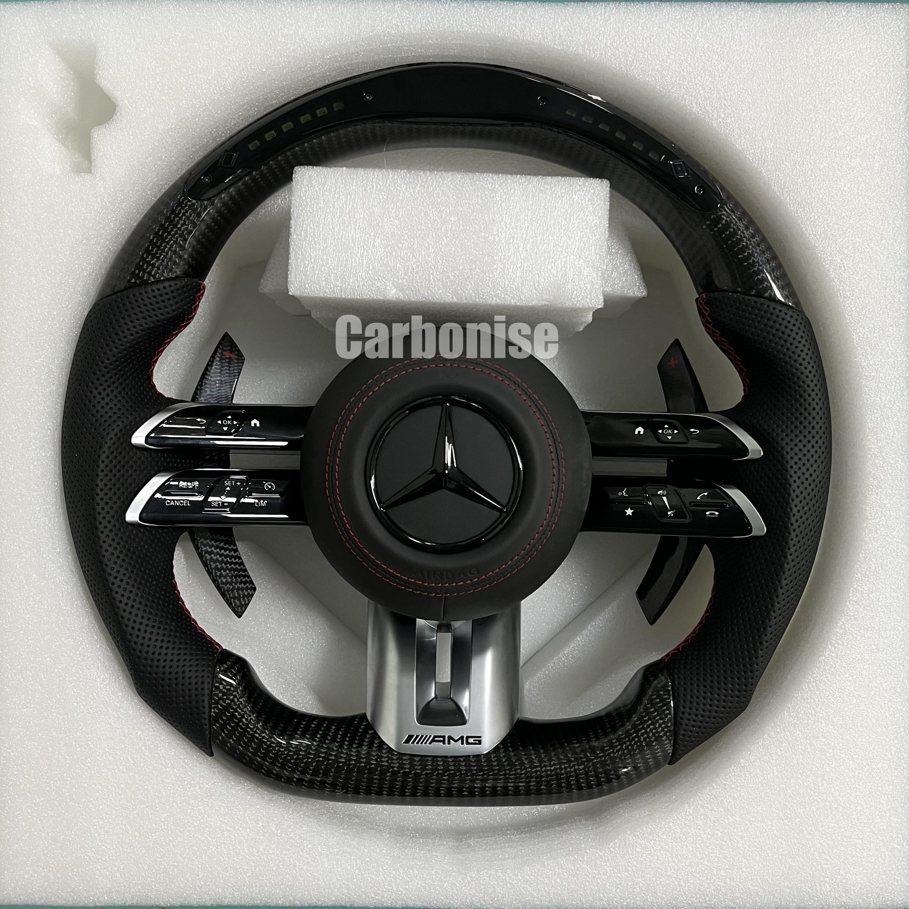 Custom Mercedes-Benz AMG performance steering wheel featuring high-gloss carbon fiber, a digital LED display, and perforated leather side grips with red stitching.