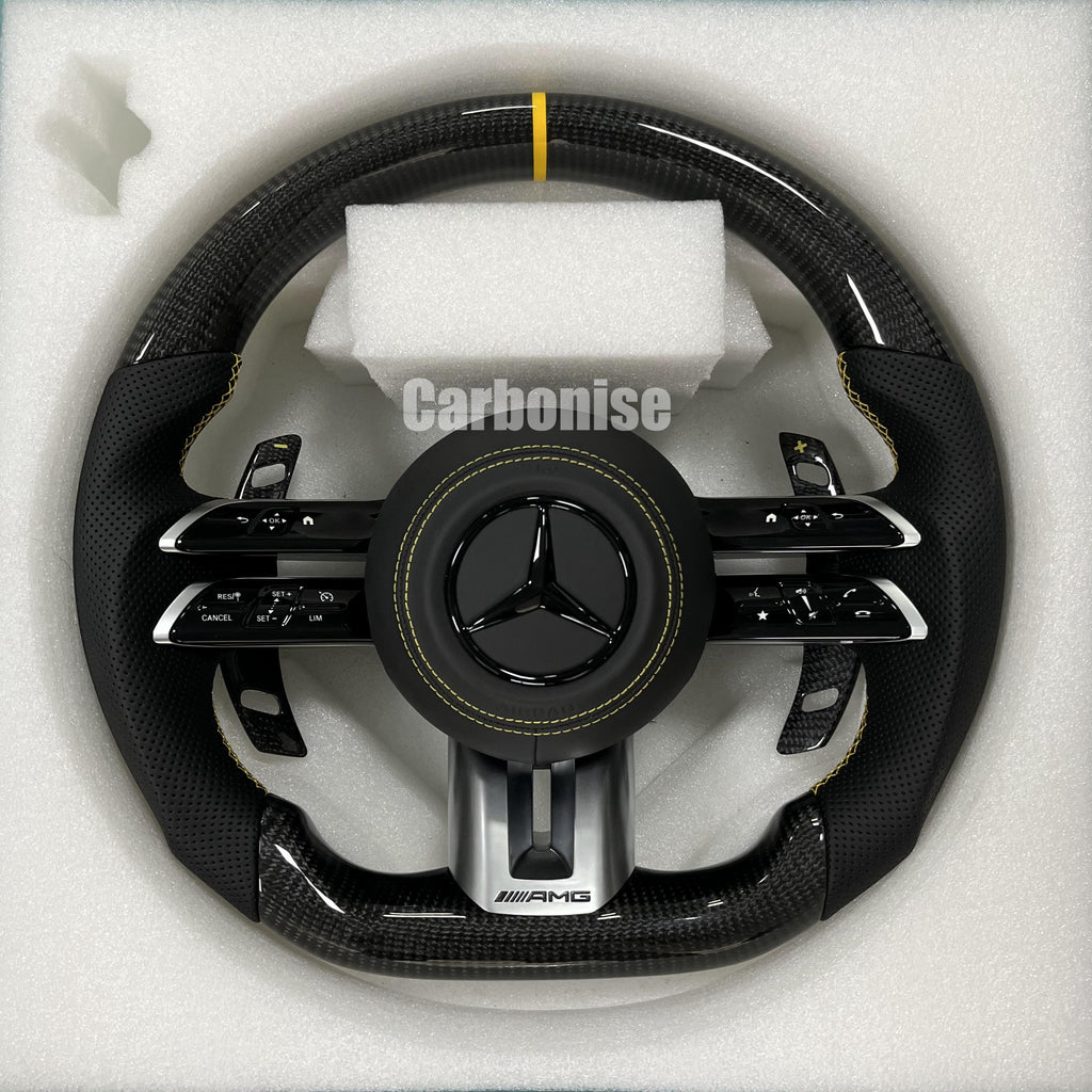 Custom Mercedes-Benz AMG steering wheel featuring high-gloss carbon fiber, a yellow top racing stripe, and black perforated leather grips with yellow stitching.