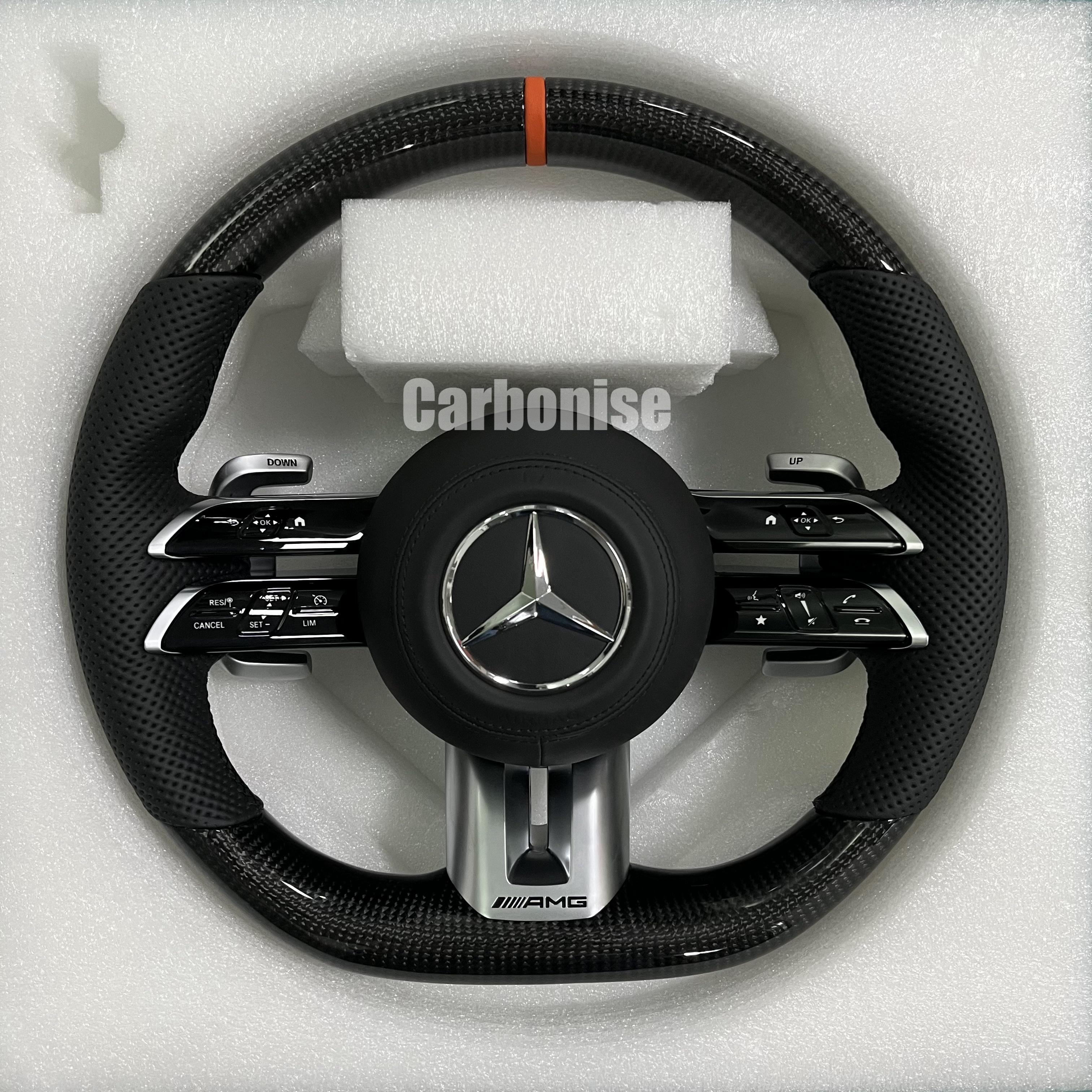 Custom Mercedes-Benz AMG steering wheel featuring high-gloss carbon fiber, a vibrant orange top racing stripe, and black perforated leather side grips.