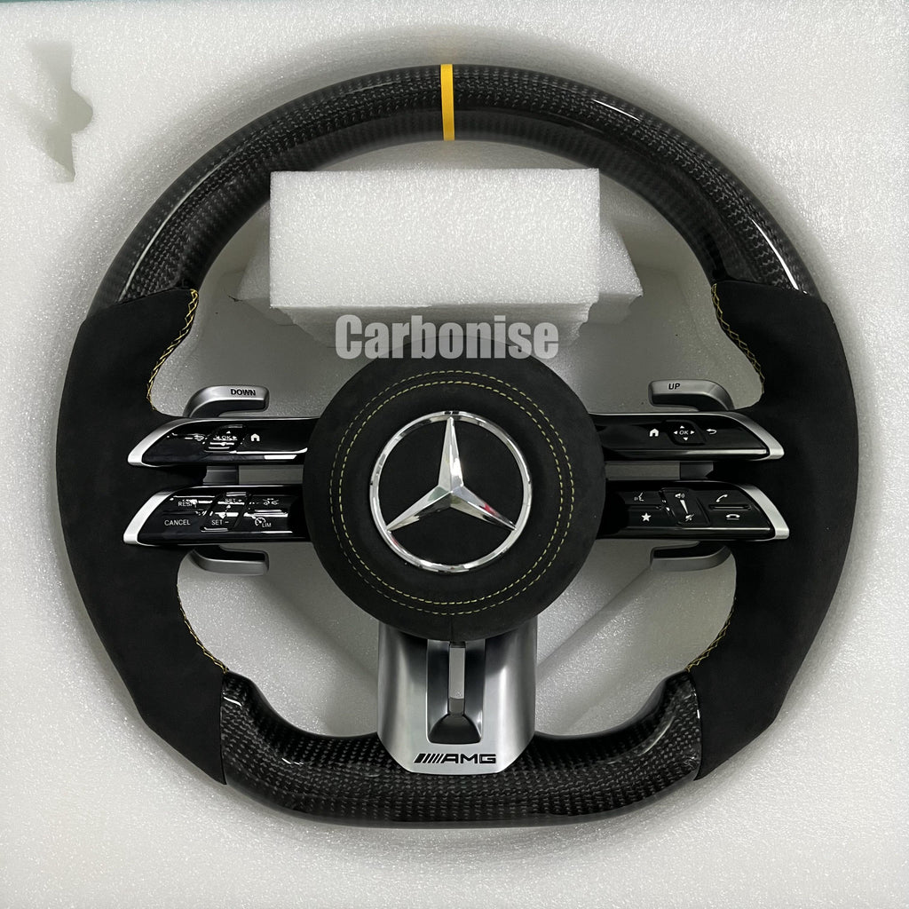 Custom Mercedes-Benz AMG steering wheel featuring high-gloss carbon fiber, a yellow top racing stripe, and black Alcantara side grips with yellow stitching.