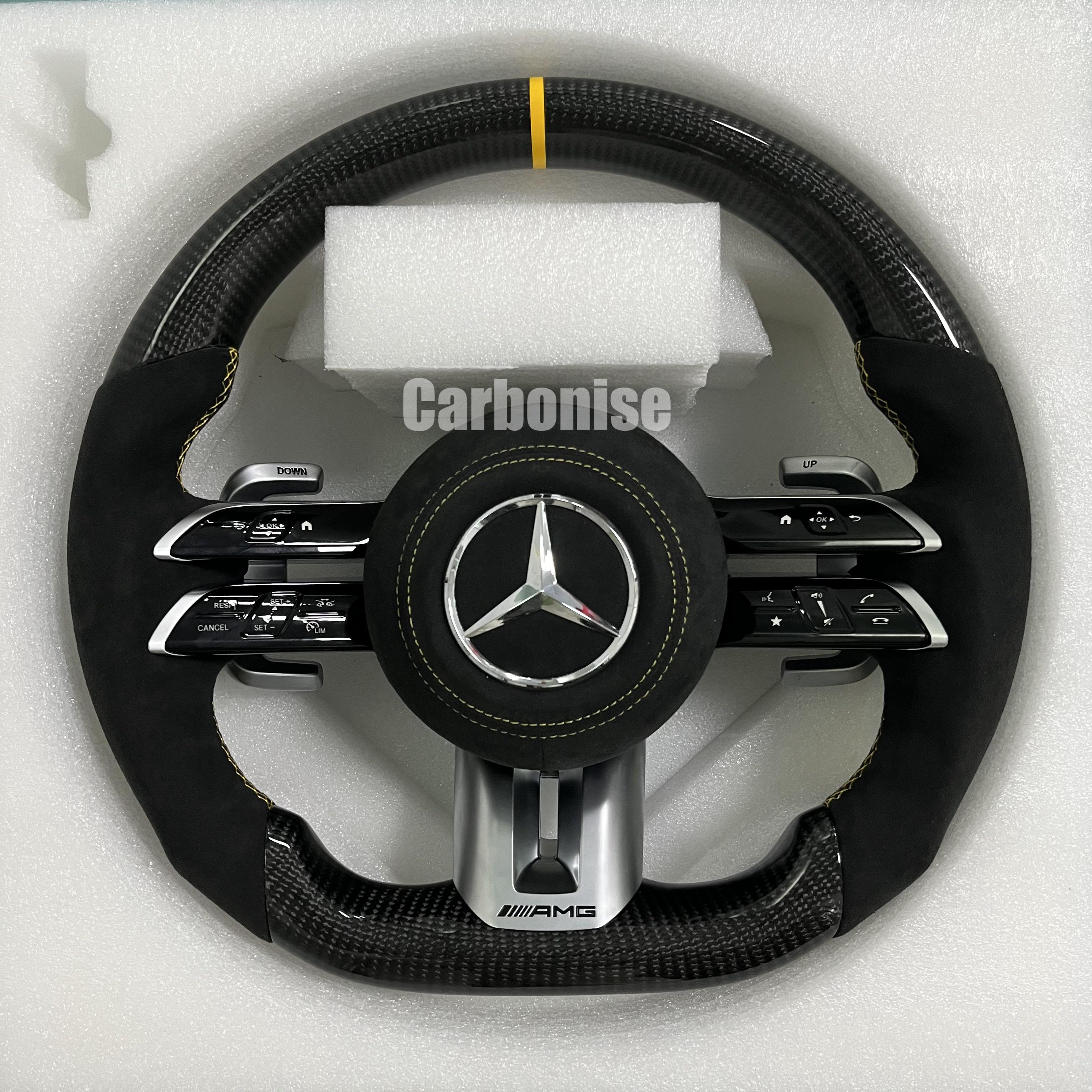 Custom Mercedes-Benz AMG steering wheel featuring high-gloss carbon fiber, a yellow top racing stripe, and black Alcantara side grips with yellow stitching.