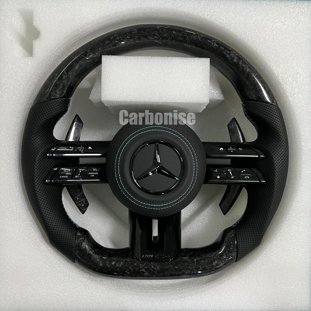 Custom Mercedes-Benz AMG steering wheel featuring high-gloss marbled forged carbon fiber, black perforated leather grips with teal stitching, and silver controls.