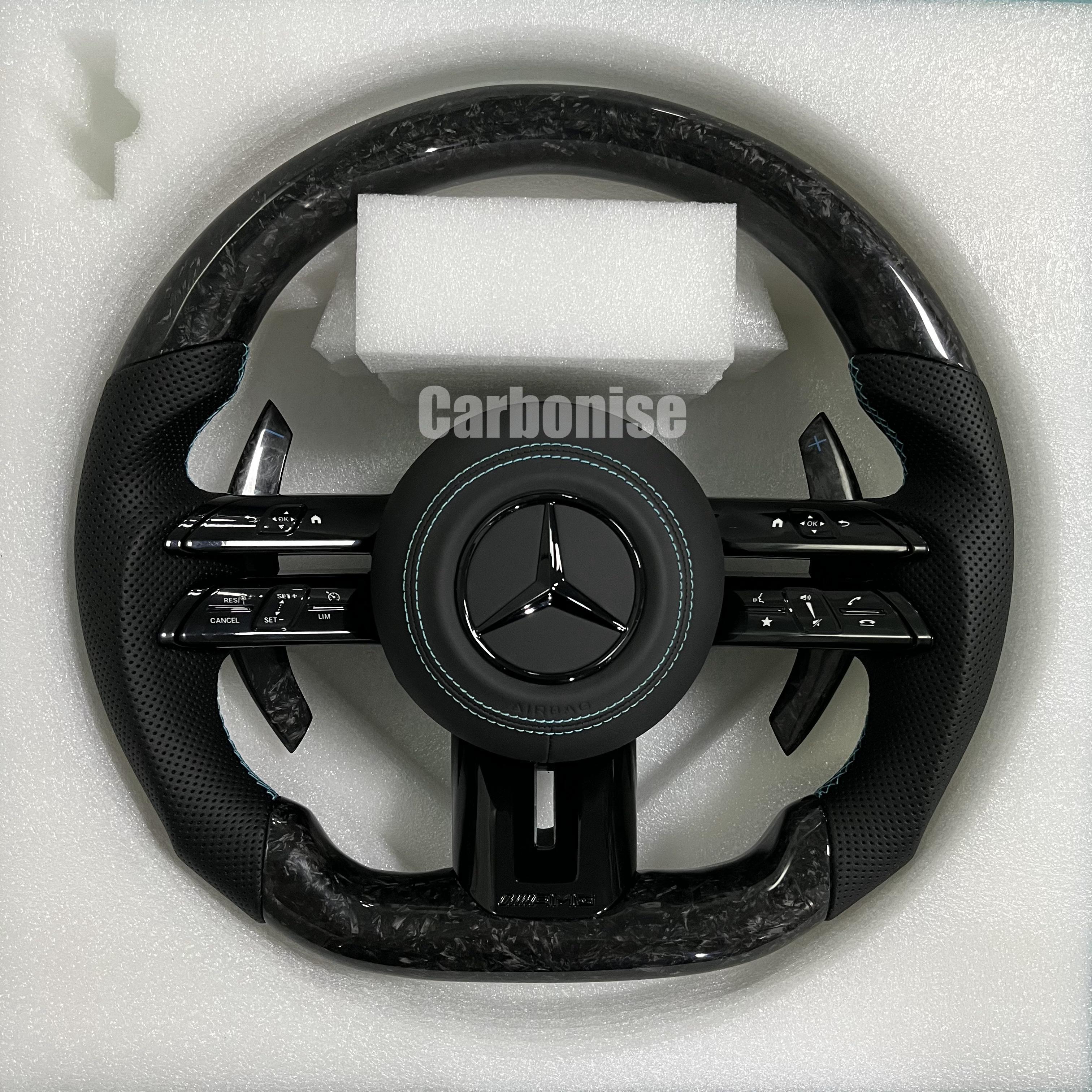 Custom Mercedes-Benz AMG steering wheel featuring high-gloss marbled forged carbon fiber, black perforated leather grips with teal stitching, and silver controls.
