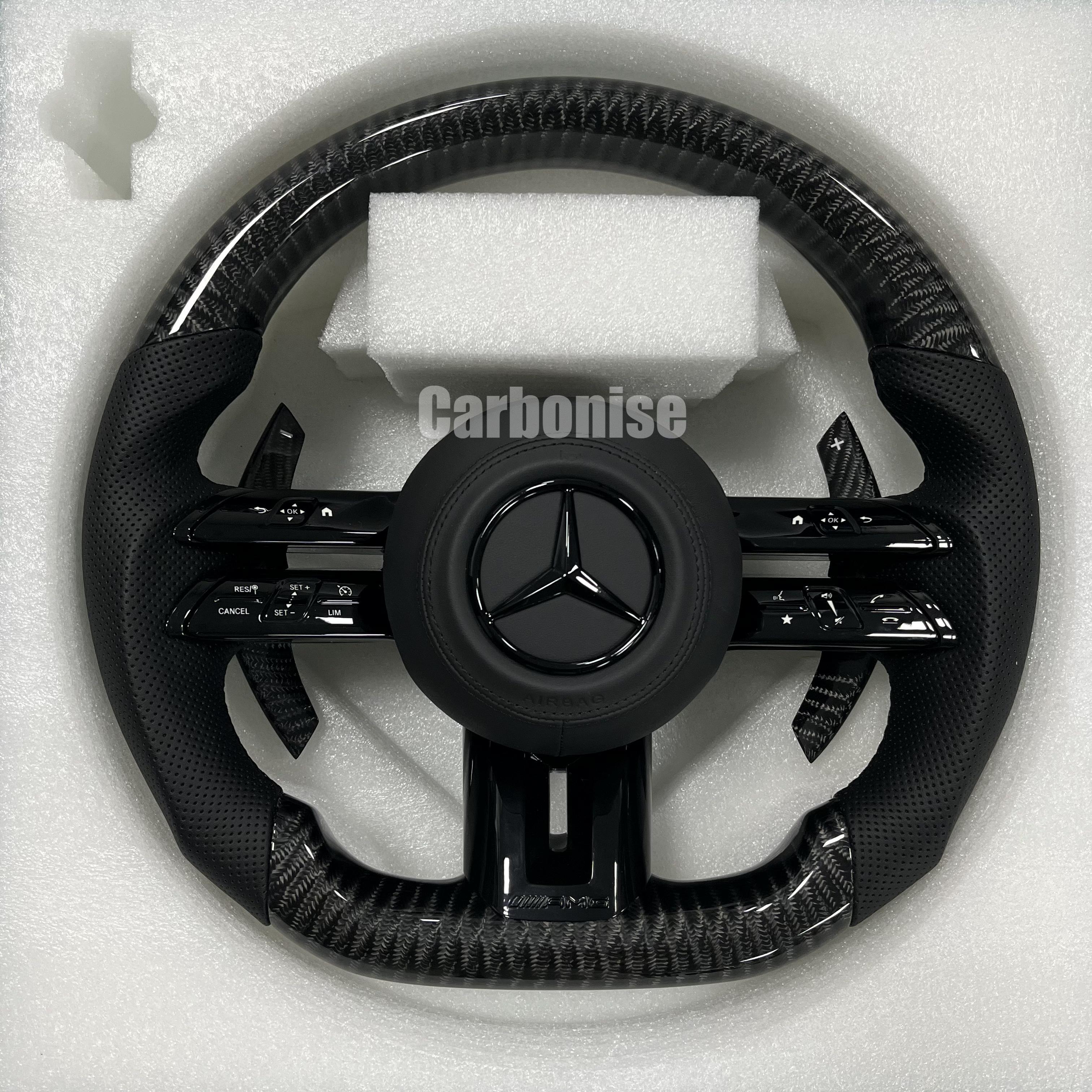 Custom Mercedes-Benz AMG steering wheel featuring high-gloss carbon fiber, black perforated leather side grips, and all-black performance controls.