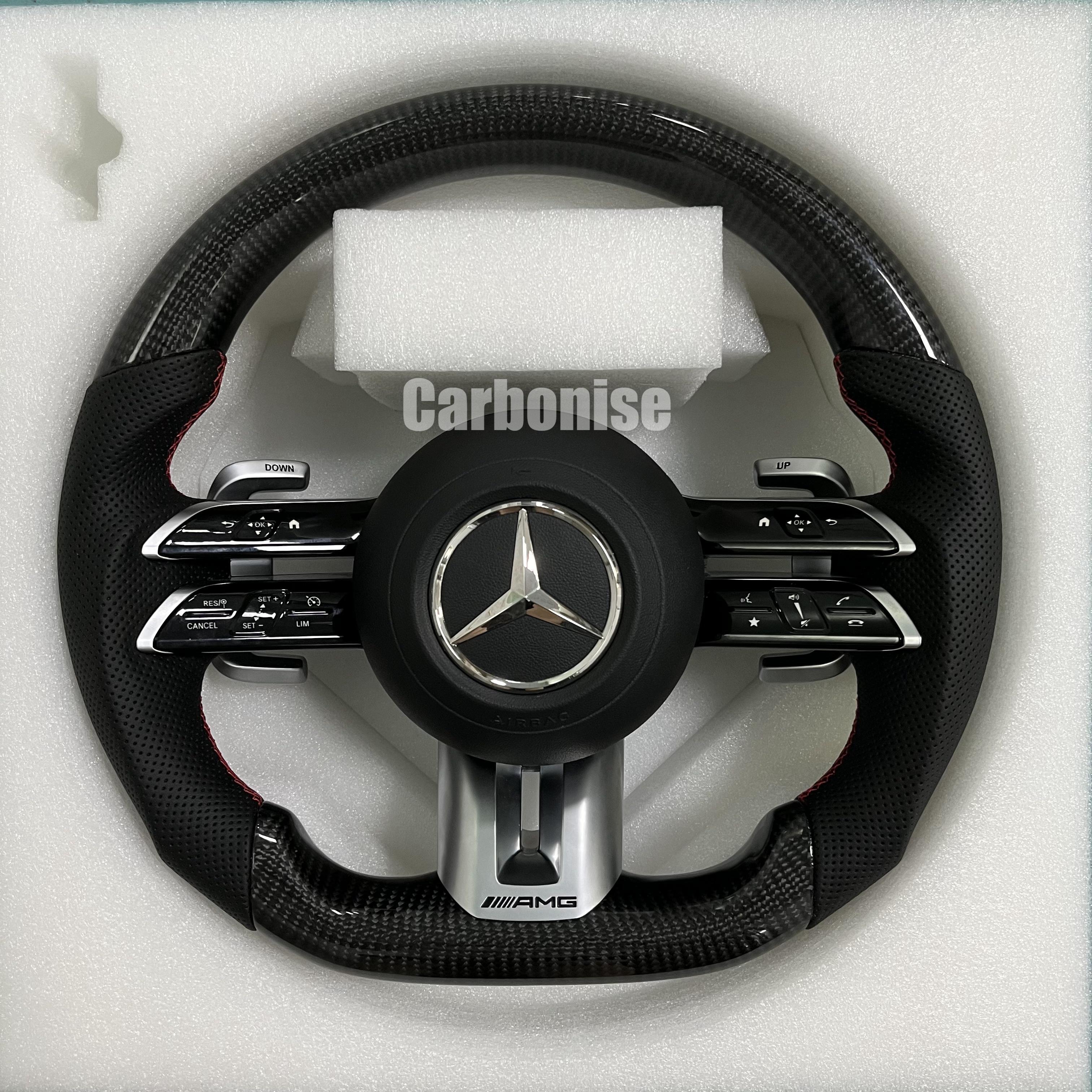 Custom Mercedes-Benz AMG steering wheel featuring high-gloss carbon fiber, black perforated leather side grips with red stitching, and silver performance controls.