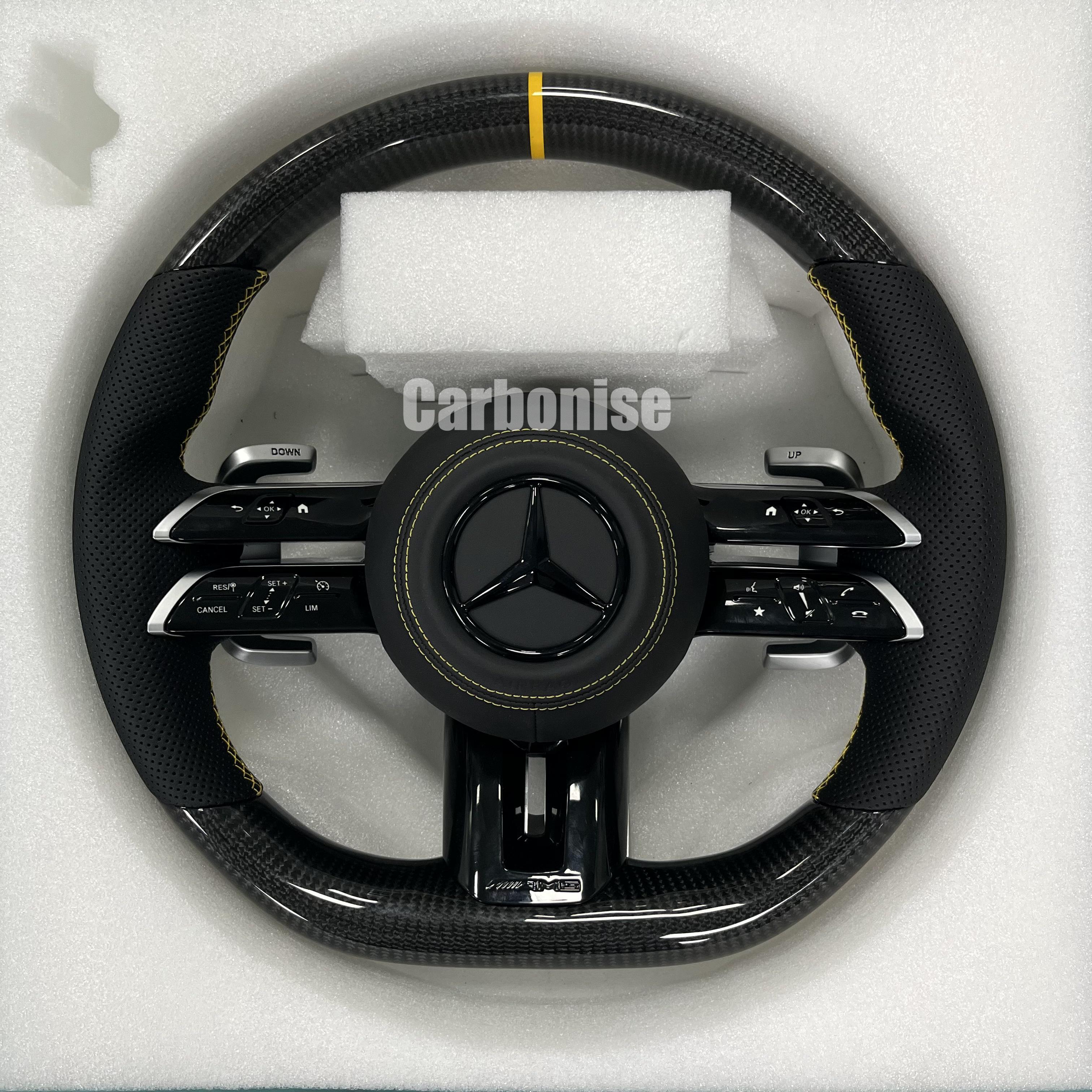 Custom Mercedes-Benz AMG steering wheel featuring high-gloss carbon fiber, a yellow top racing stripe, and black perforated leather grips with yellow stitching.