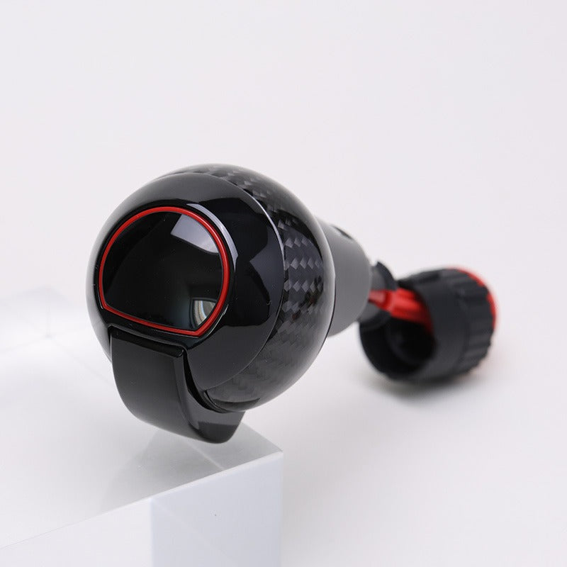 Carbon fibre gear shift knob with gloss black finish, red accent ring, and rounded performance design.