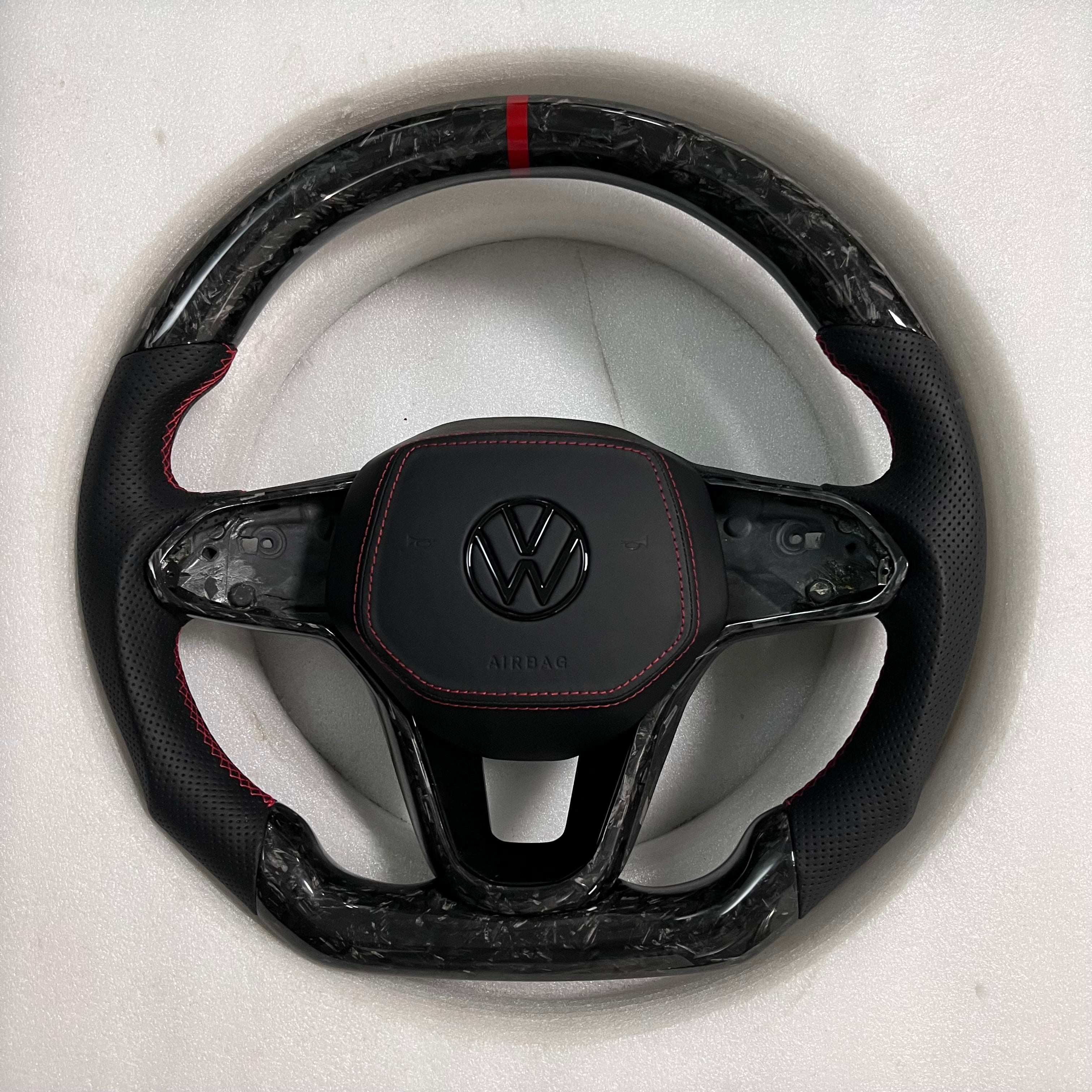 Custom Volkswagen performance steering wheel featuring high-gloss marbled forged carbon fiber, a red top racing stripe, and black perforated leather side grips with red stitching.