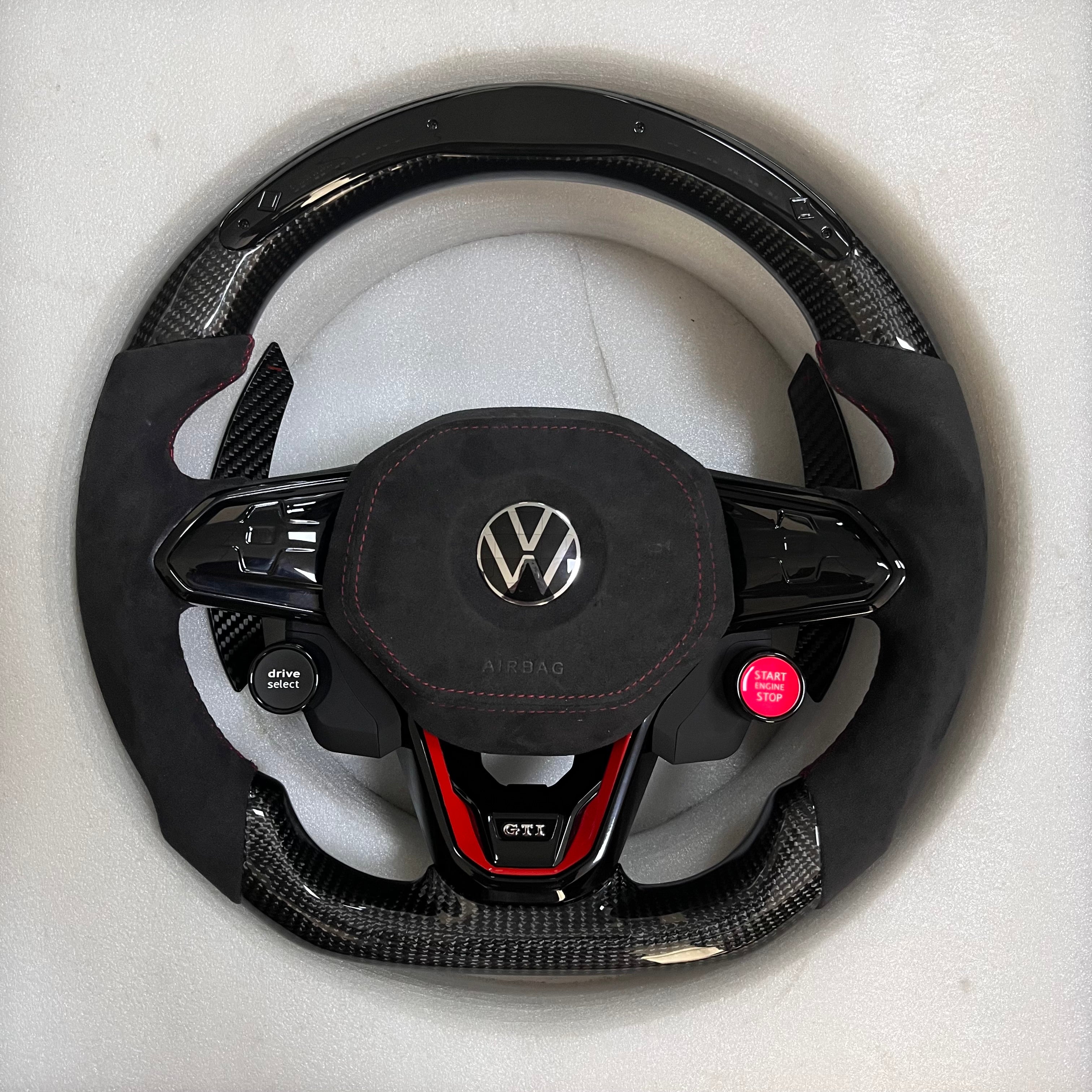 Custom Volkswagen performance steering wheel featuring high-gloss carbon fiber, black Alcantara side grips, and integrated R8-style red start/stop buttons.