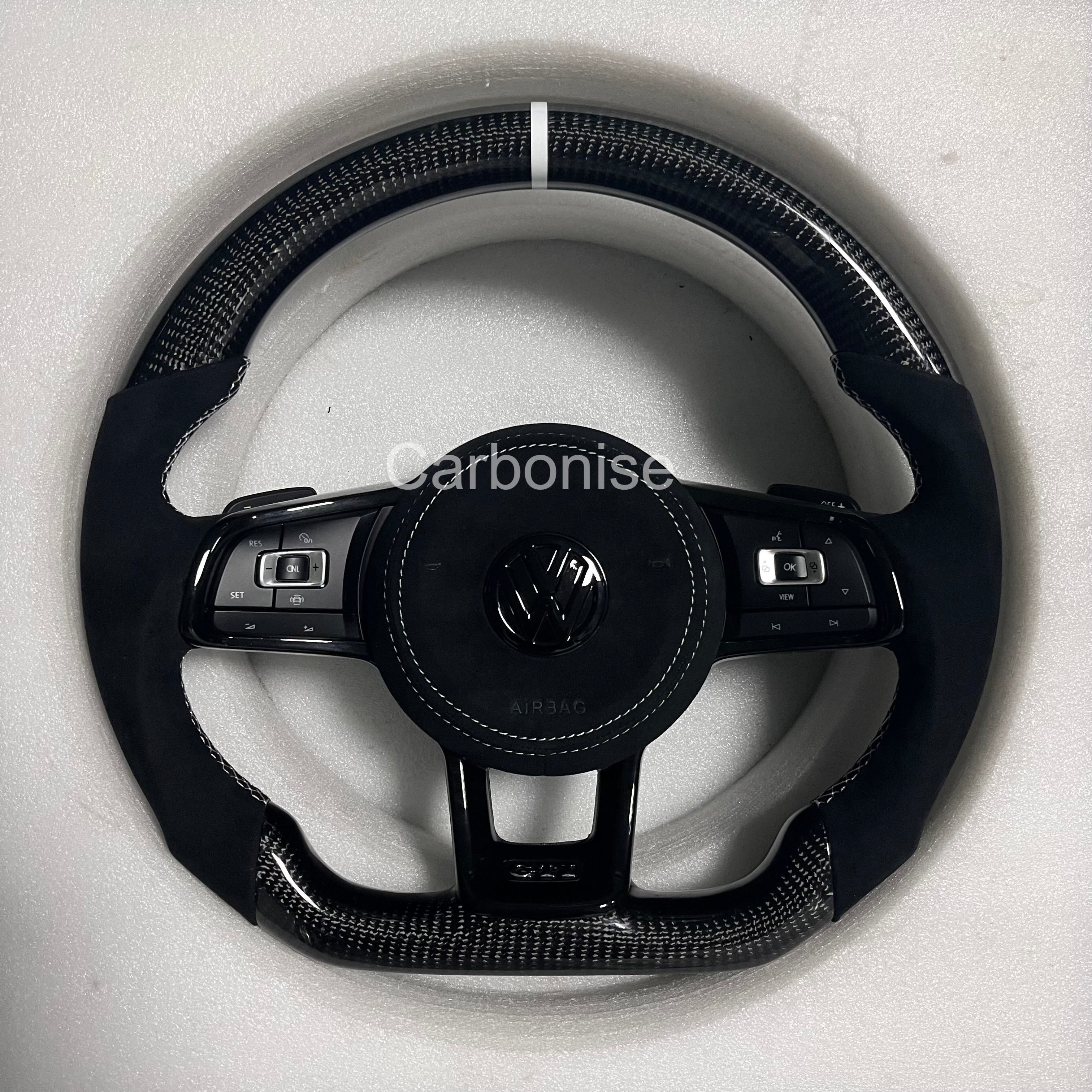 Custom Volkswagen performance steering wheel featuring high-gloss carbon fiber, a white top racing stripe, and black Alcantara side grips.