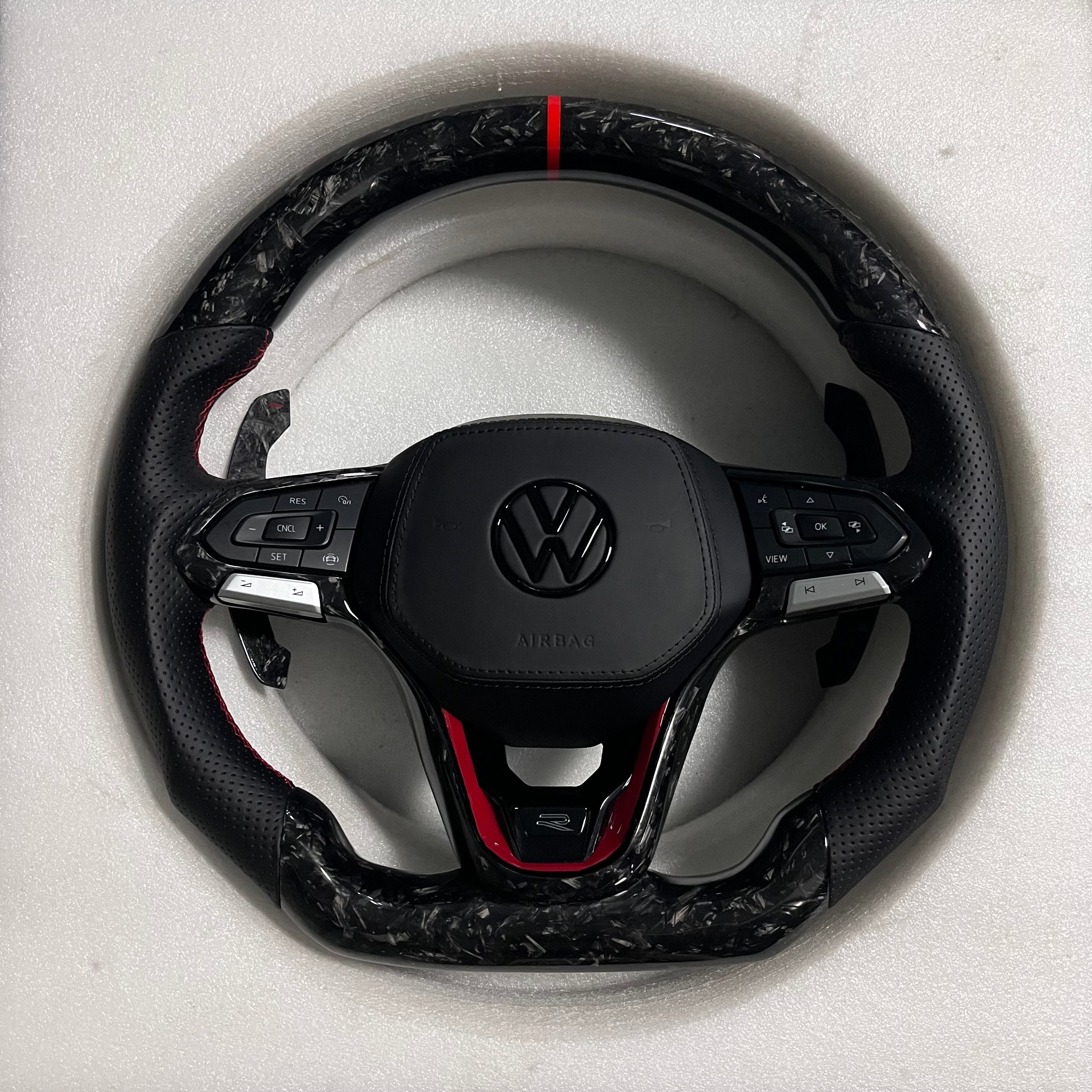 Custom Volkswagen performance steering wheel featuring high-gloss marbled forged carbon fiber, a red top racing stripe, and black perforated leather grips with red stitching.