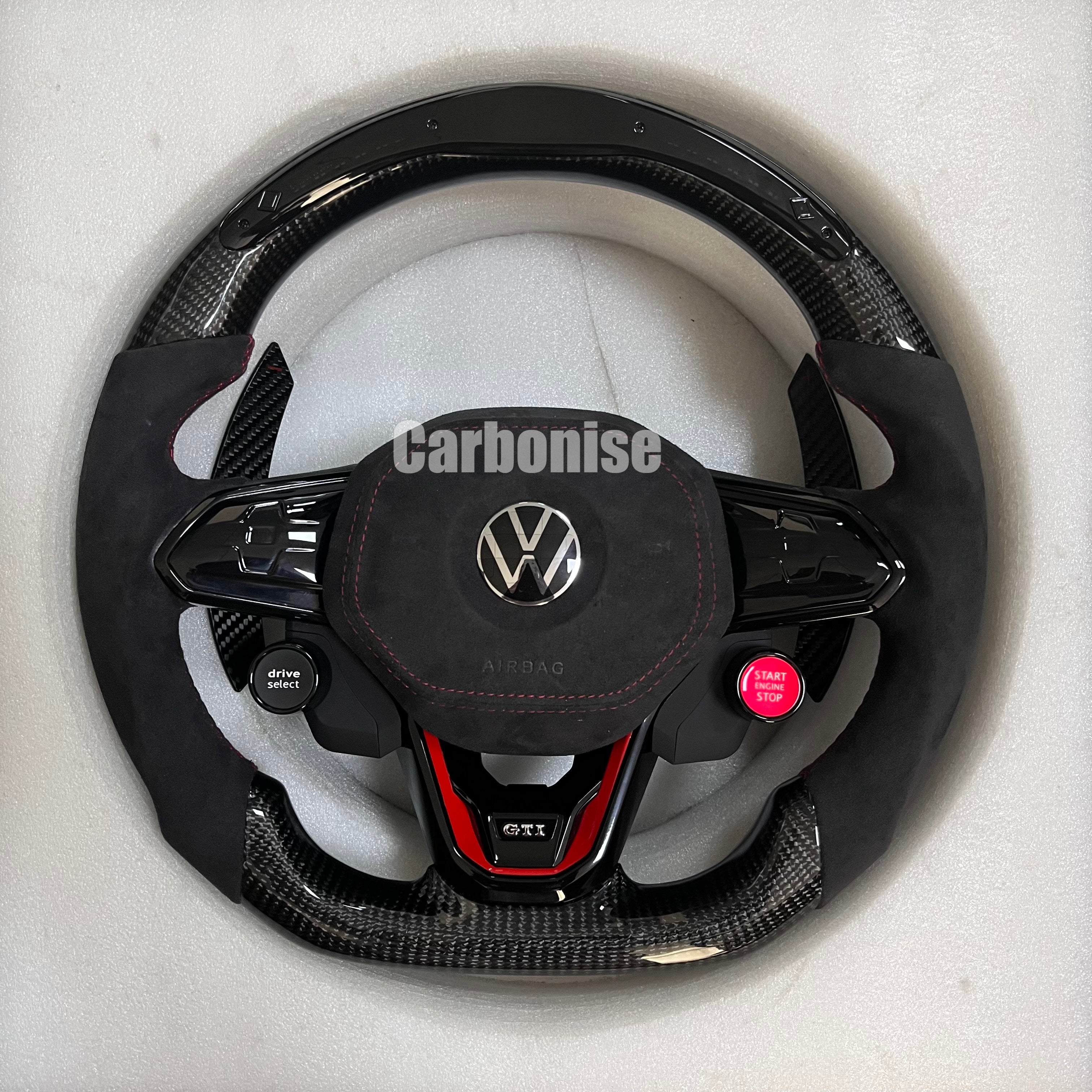 Custom Volkswagen performance steering wheel featuring high-gloss carbon fiber, black Alcantara side grips, and integrated R8-style red start/stop buttons.