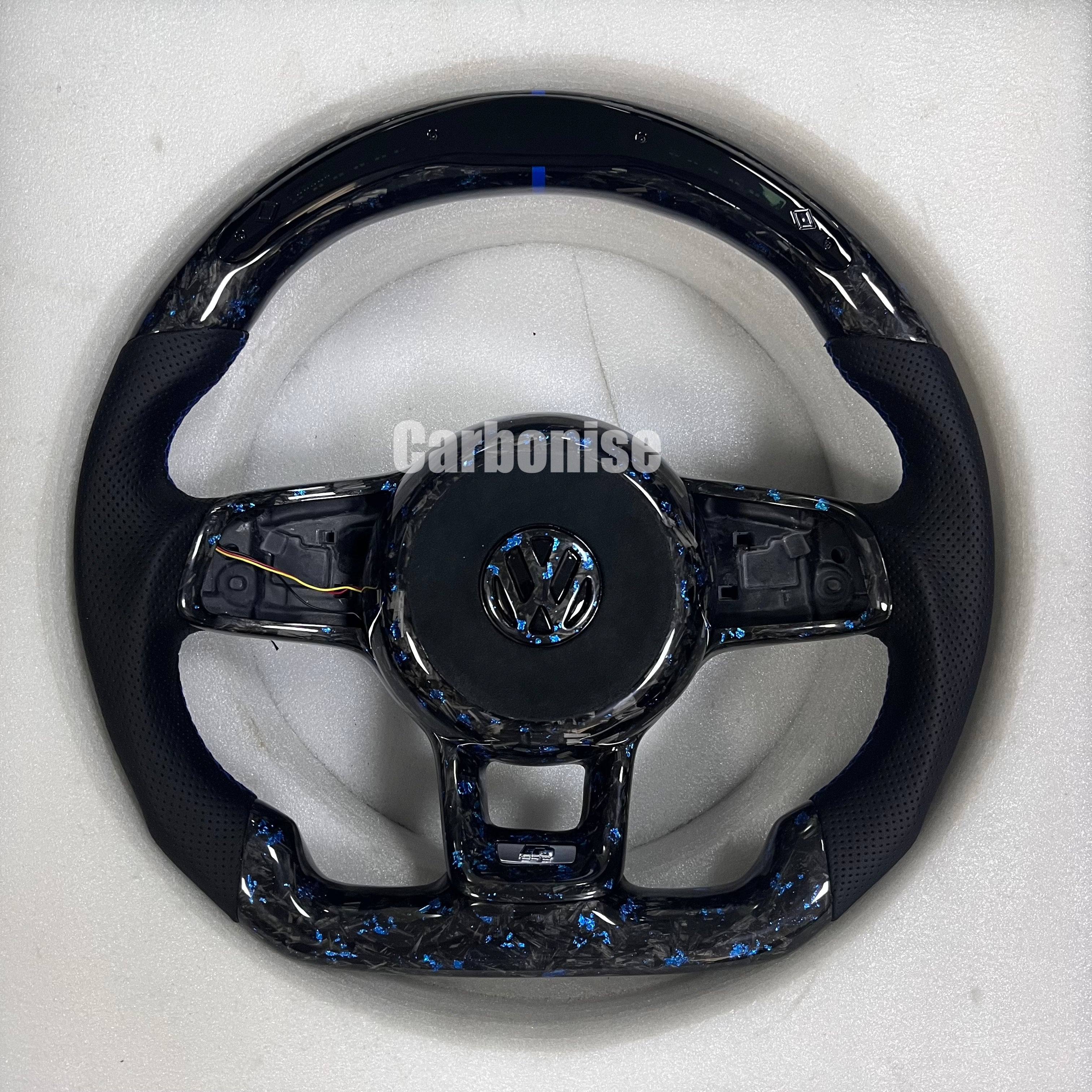 Custom Volkswagen performance steering wheel featuring forged carbon fiber with blue flakes, a blue top racing stripe, and black perforated leather side grips.